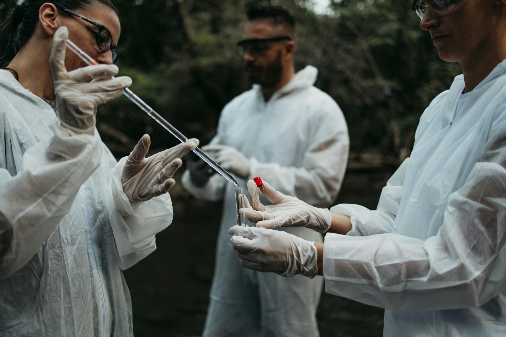 Three people in white protective suits with scientific equipment.