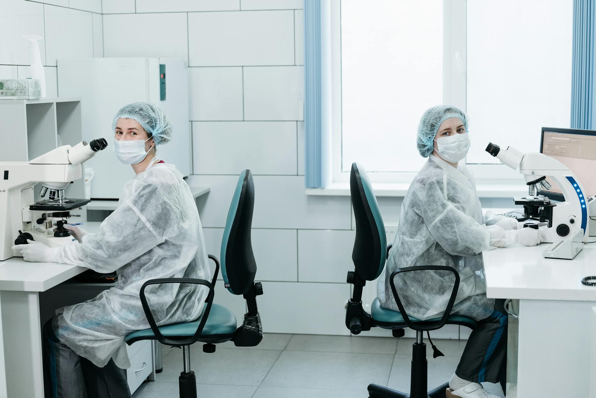two scientists wearing full protective gear looking at samples through a microscope