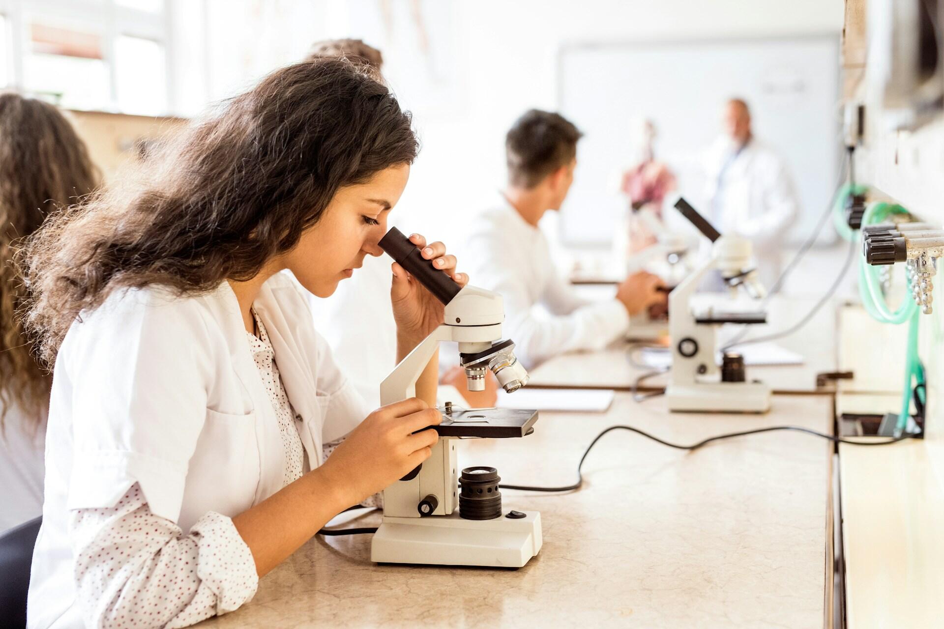 People in labcoats use microscopes.