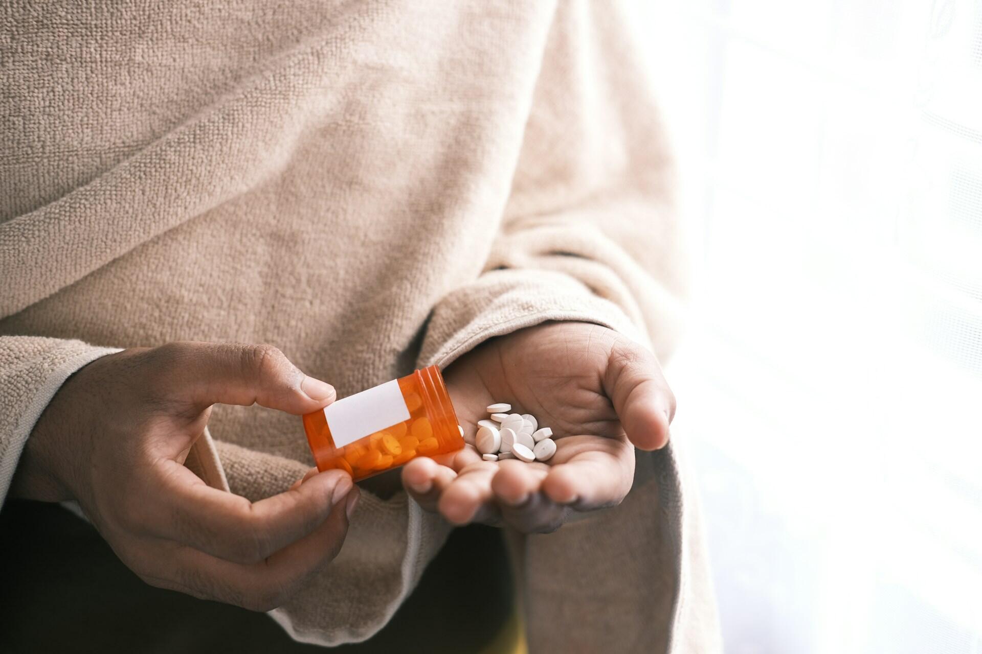 A person holding a pill jar and pills in their hand.