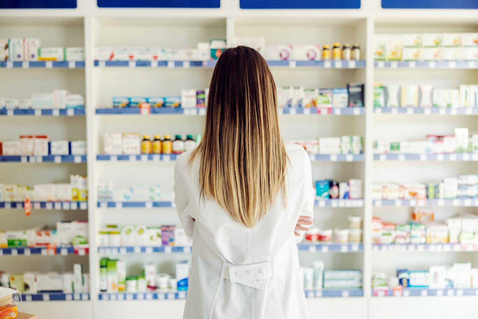 A person in a lab coat looking at shelves in a pharmacy.