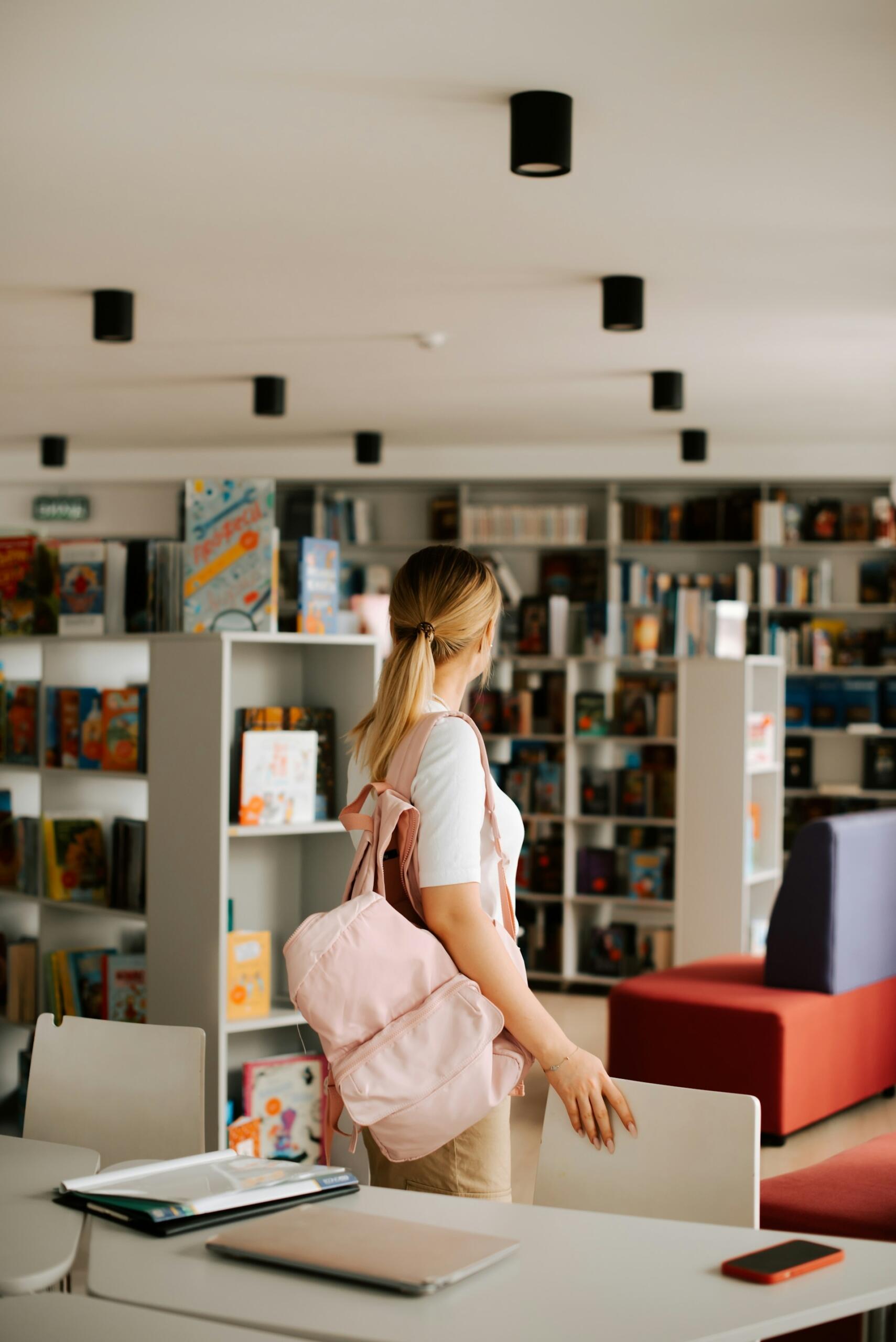 A woman in a library with a pink bag.