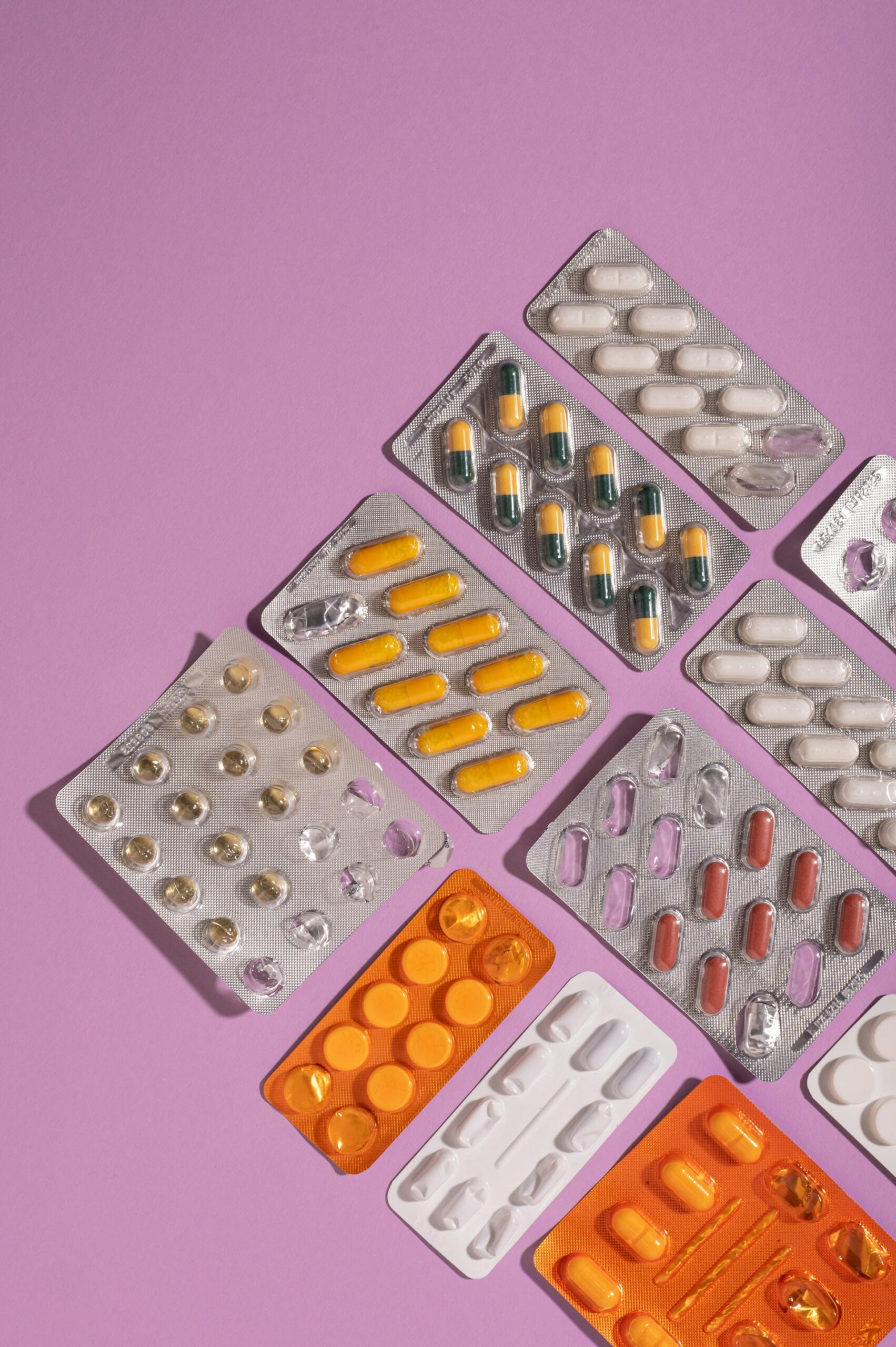 A variety of colorful medication blister packs arranged on a pastel purple background.