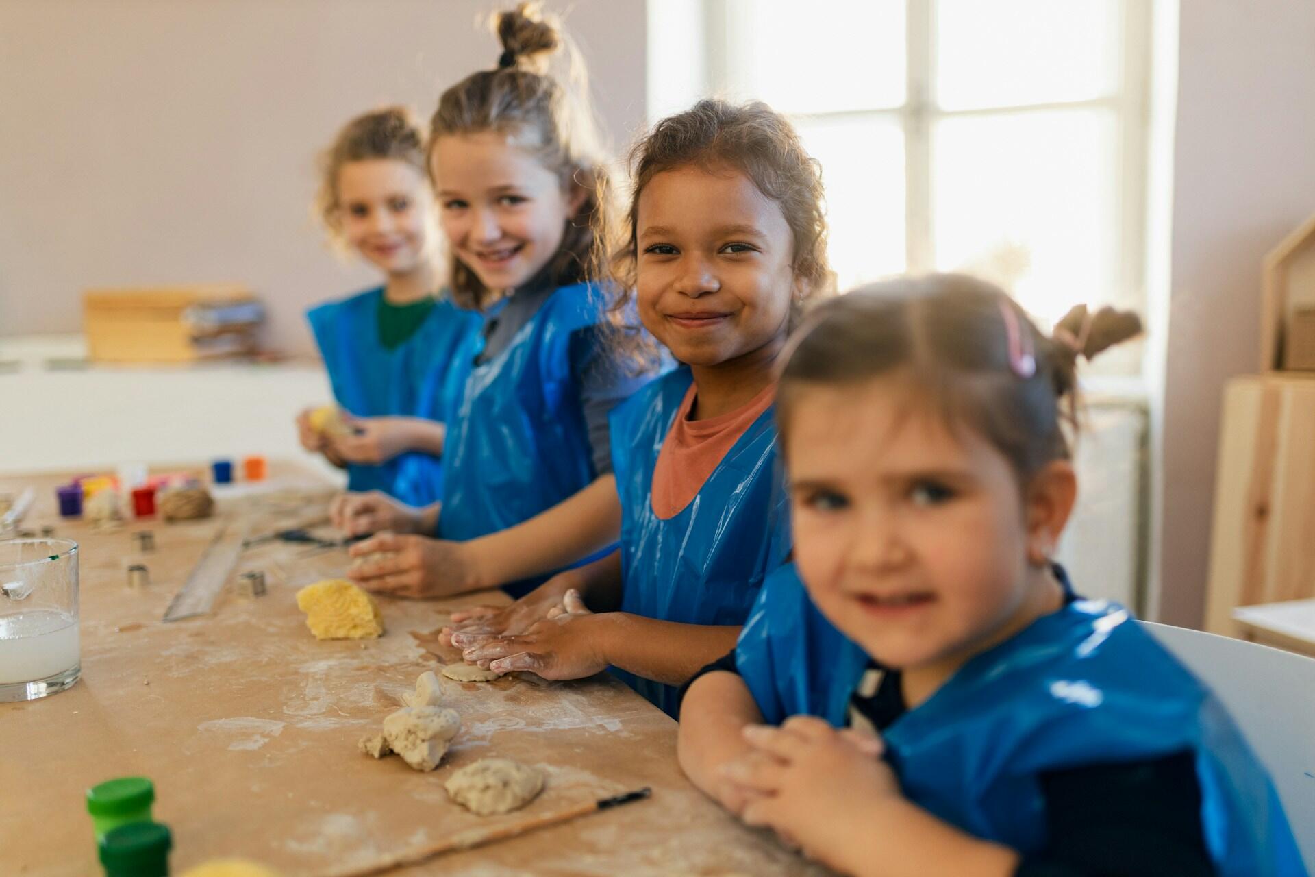Four children in blue pinafores at an art table.