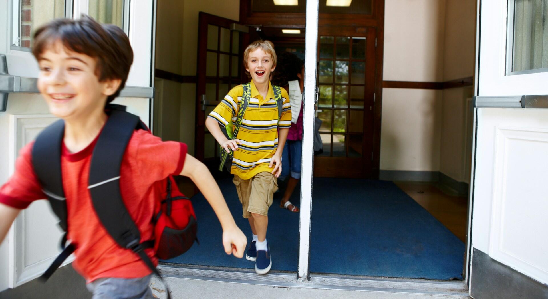 Two boys wearing backpacks run out of a building.