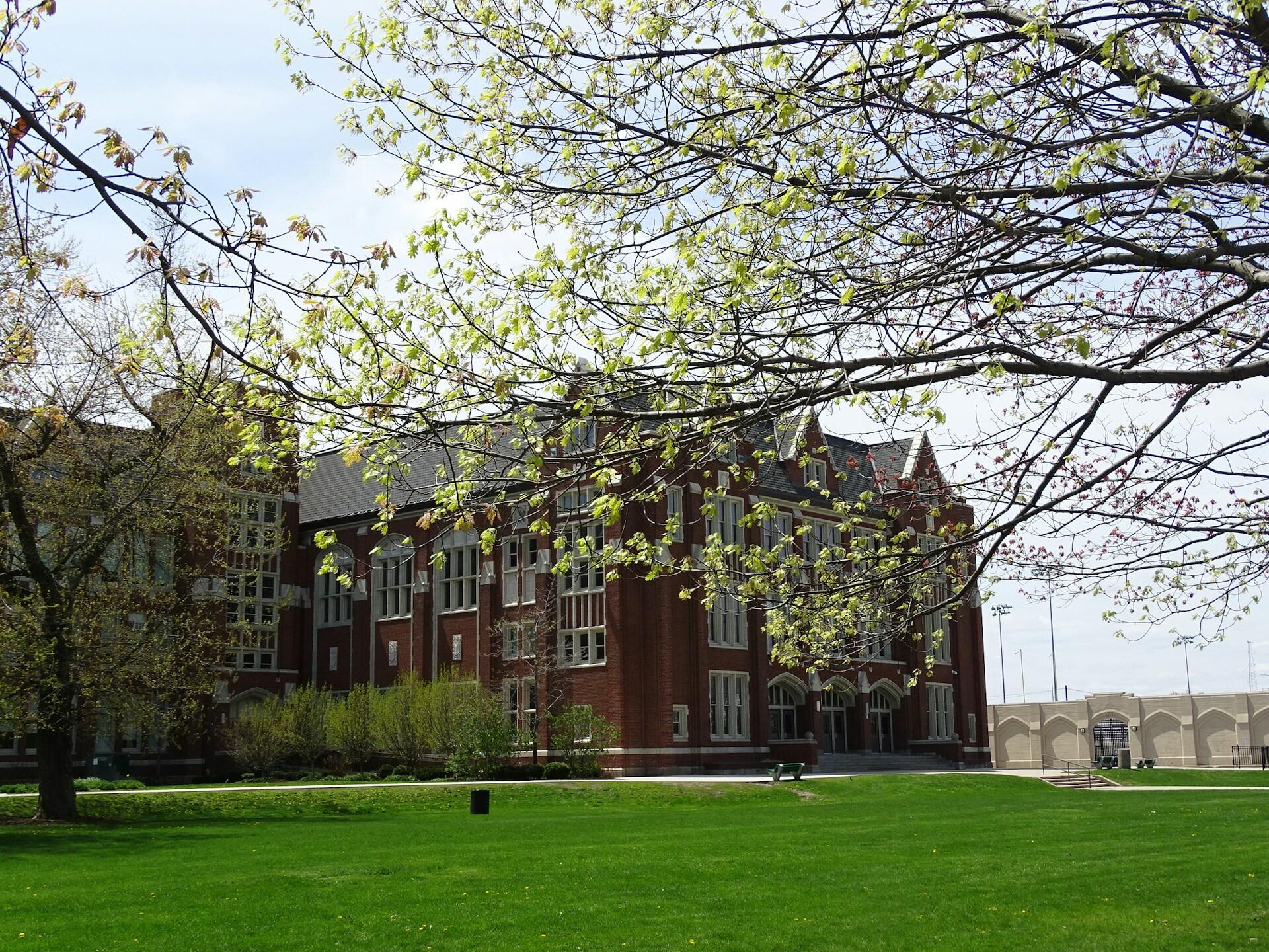 A school campus with a stone building in front of a wide green space.