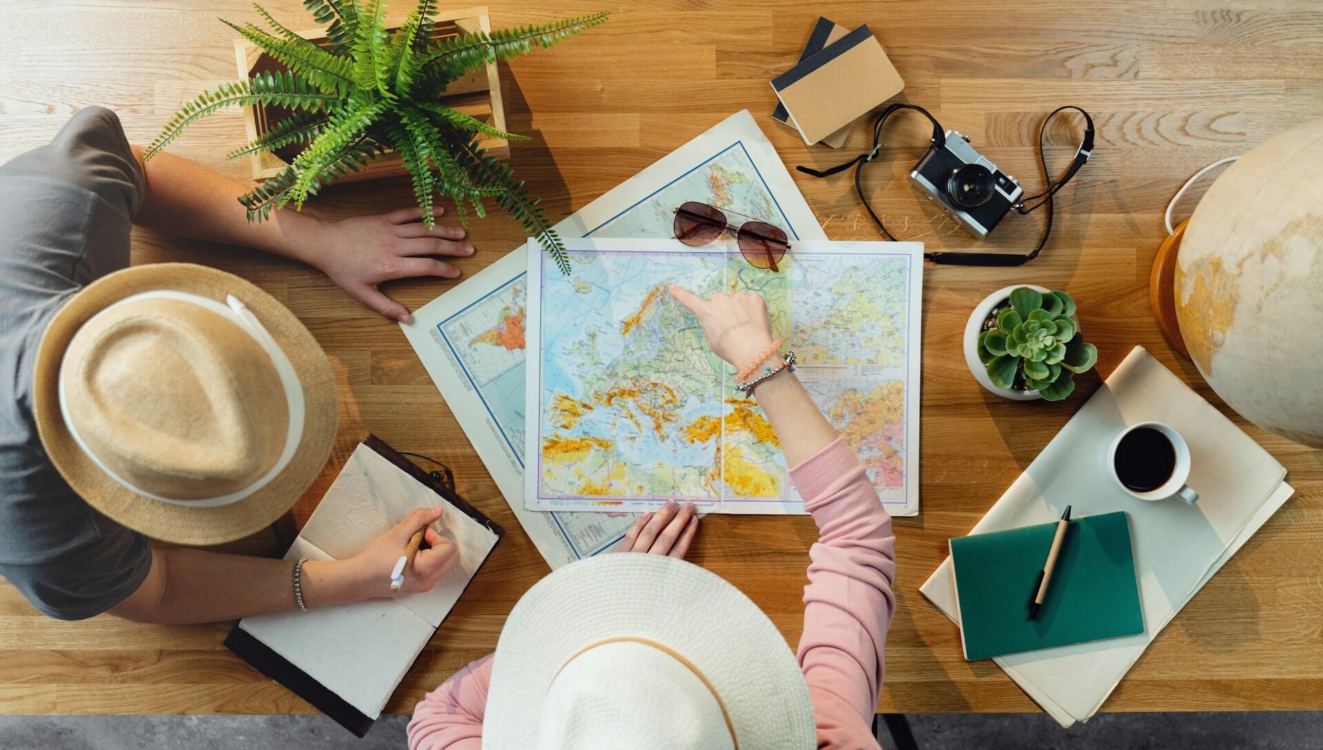 Two people discussing and pointing at maps on a wooden table.