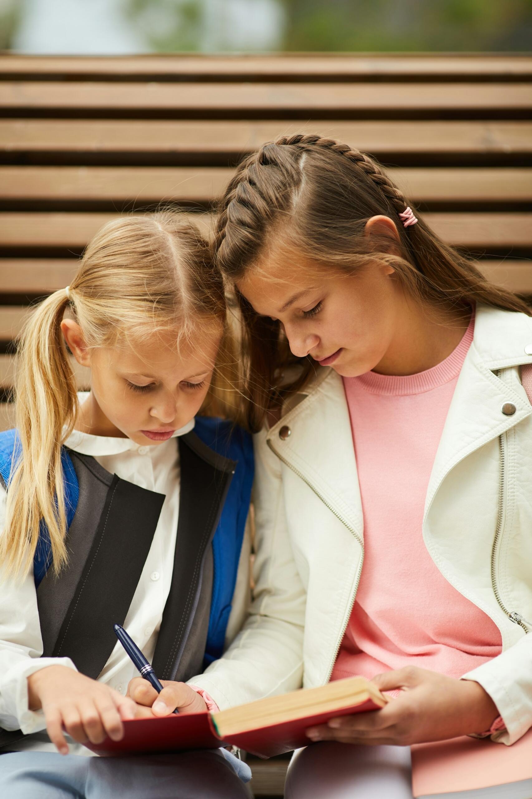 An older student shows a younger one a notebook. 