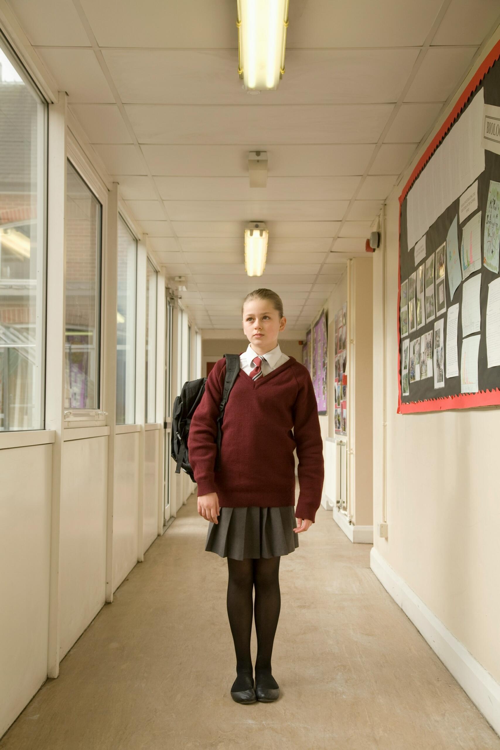 A girl stands in a hallway wearing a school uniform.