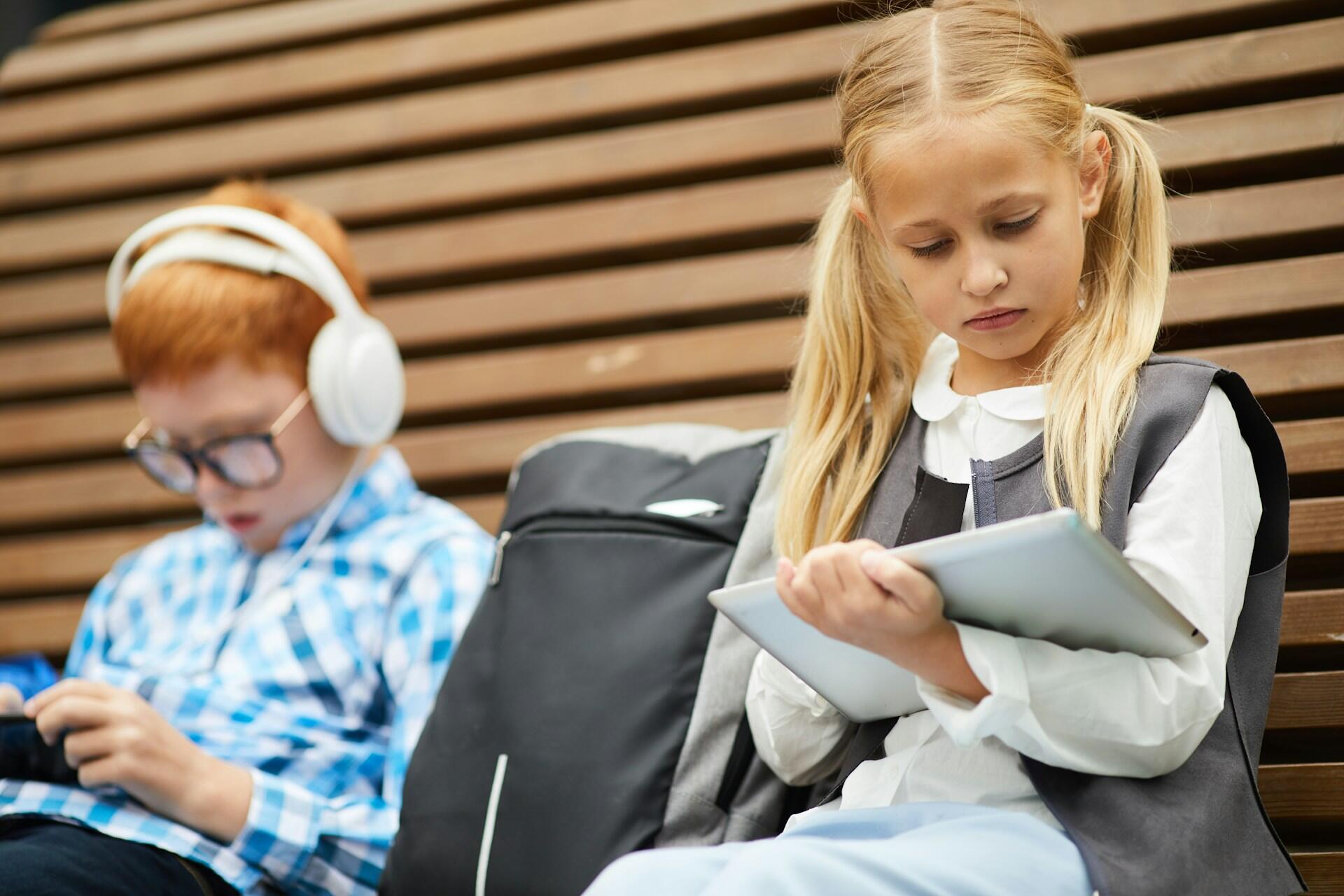 A girl wearing a grey school vest sitting on a bench. 