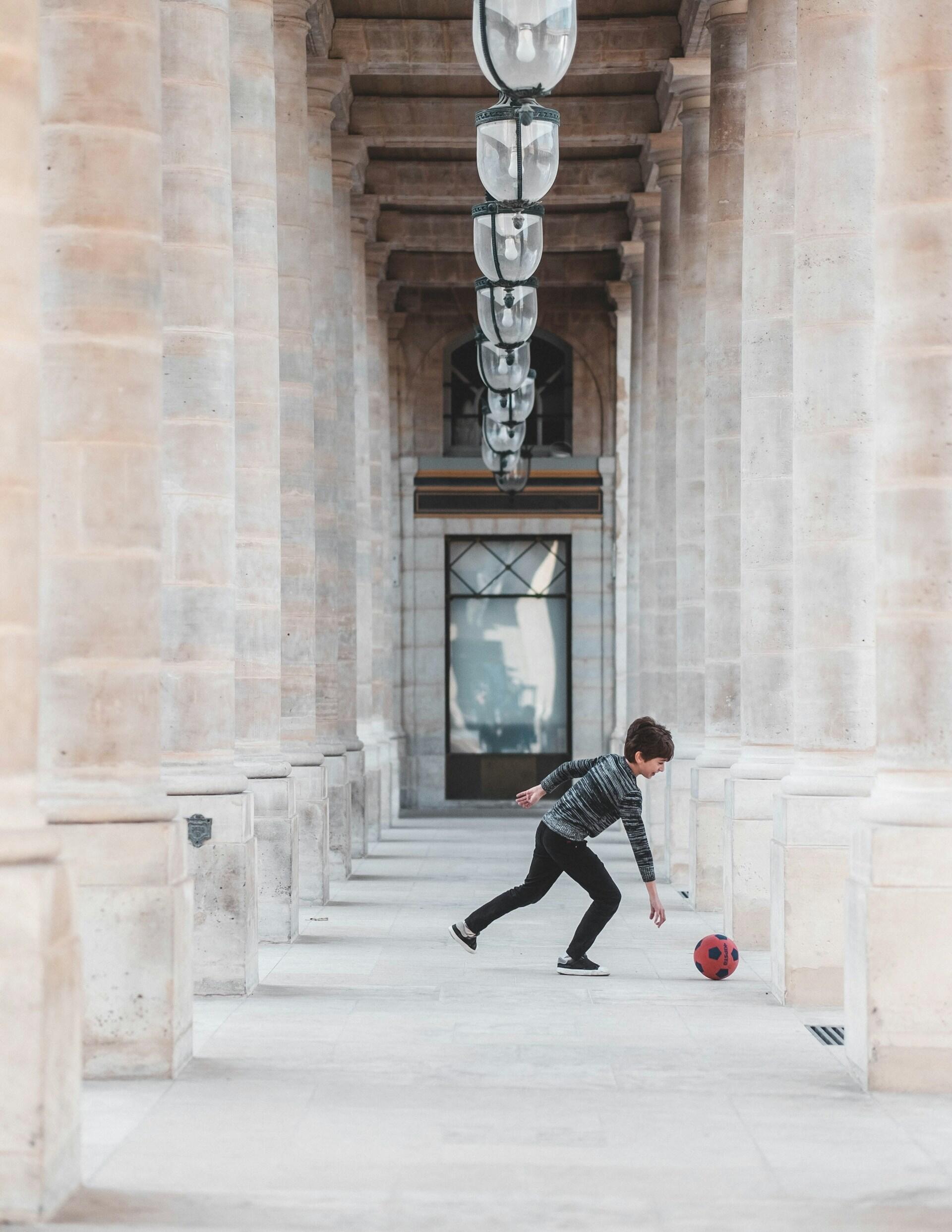A child plays ball on an arched walkway.