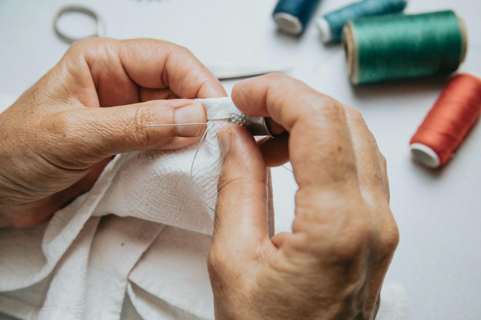 A person sewing by hand with a thimble.
