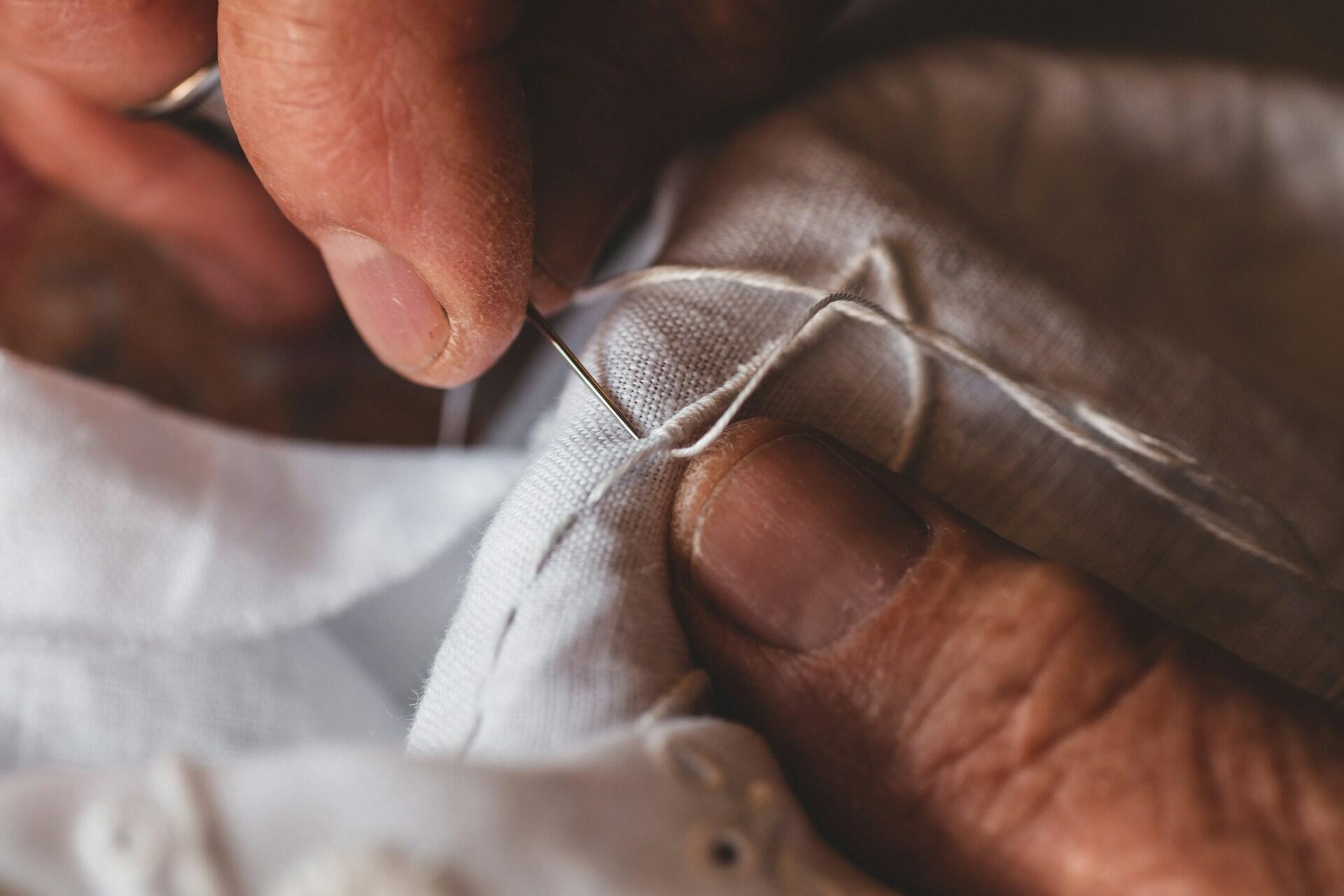 A close up of hands plying a sewing needle into white fabric.