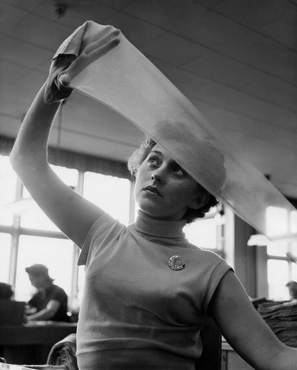 A woman holds a Nylon sock against the light to examine the quality.