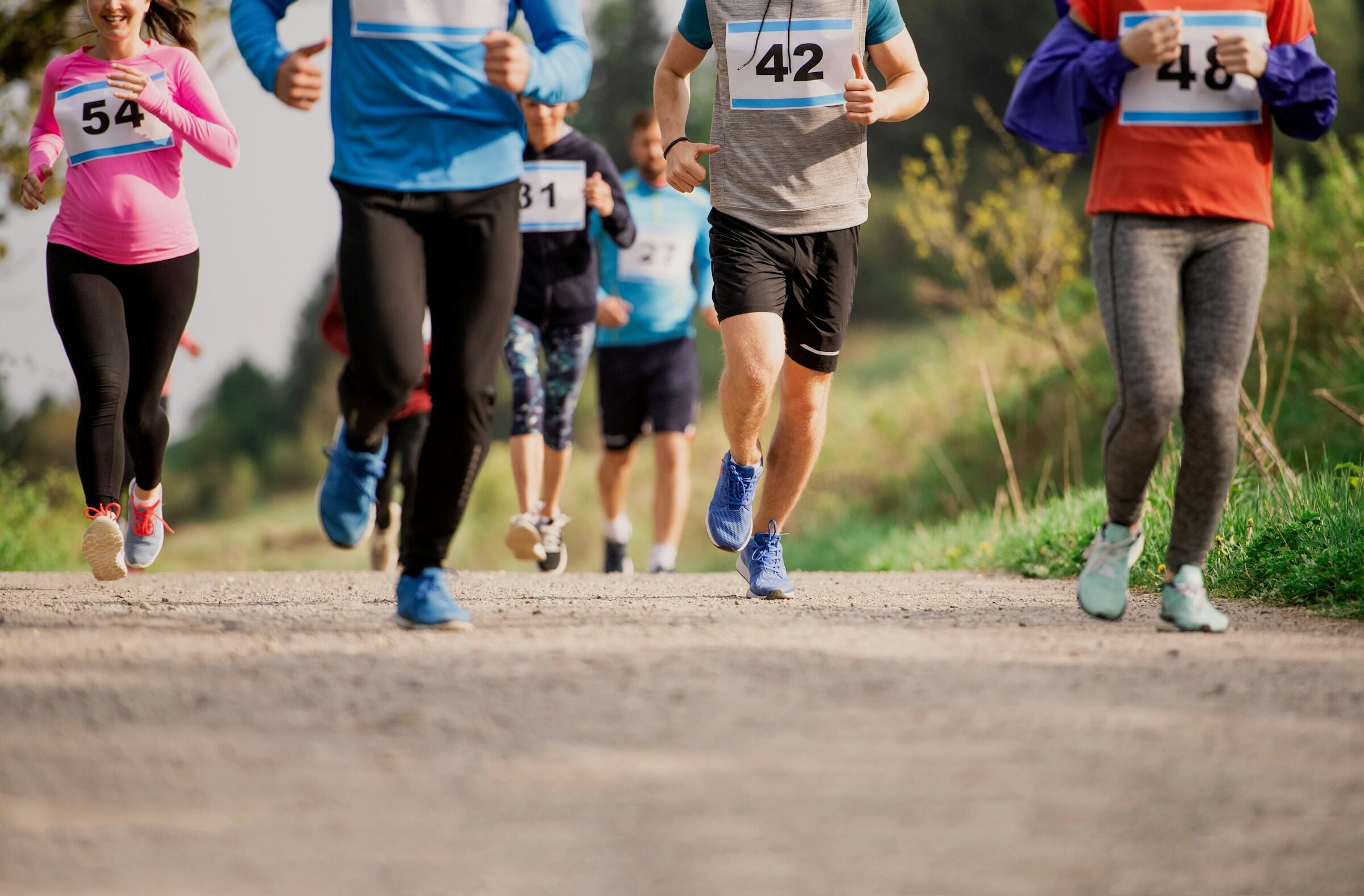 A group of runners in colorful athleticwear race down a gravel path.