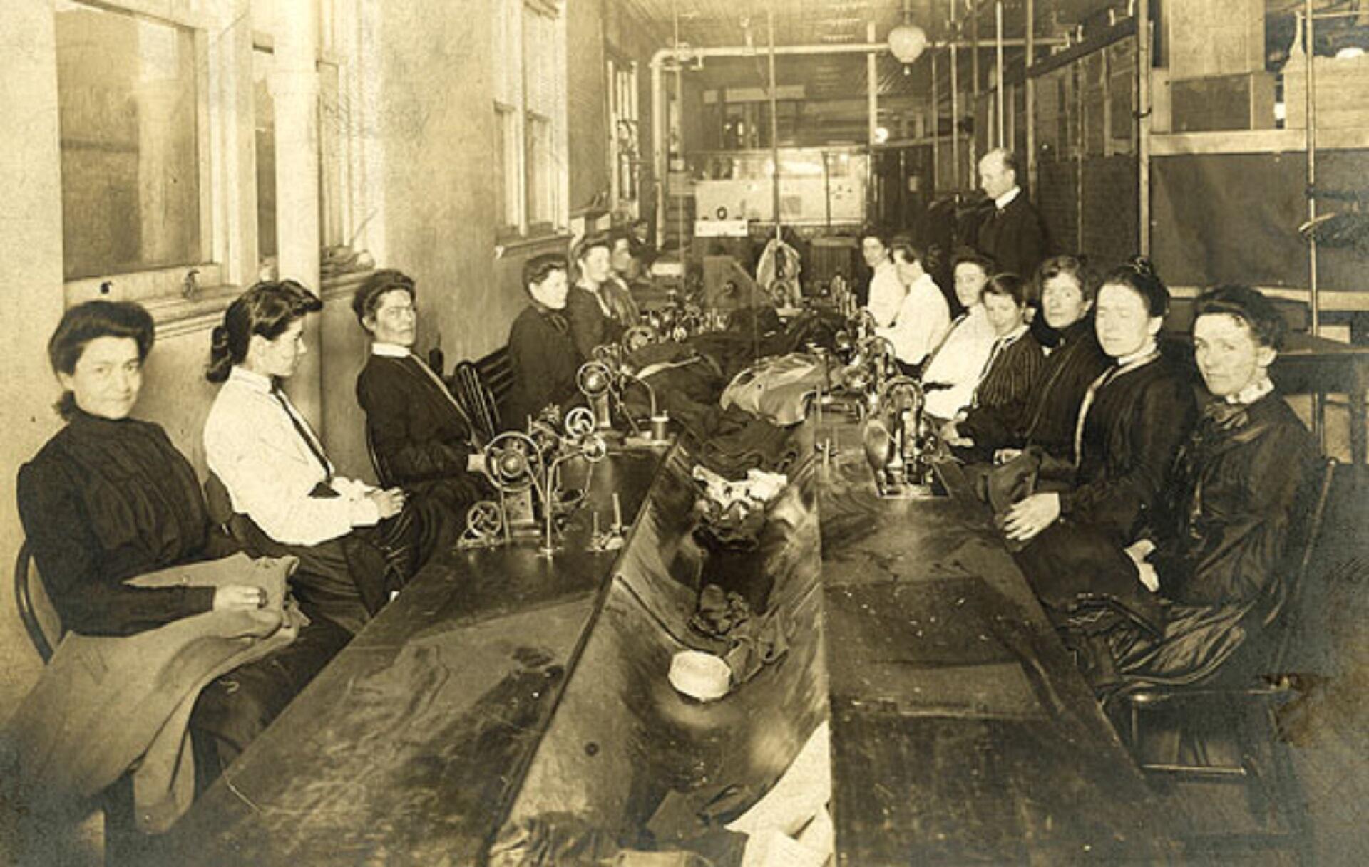 Women sitting at a long table in front of sewing machines.
