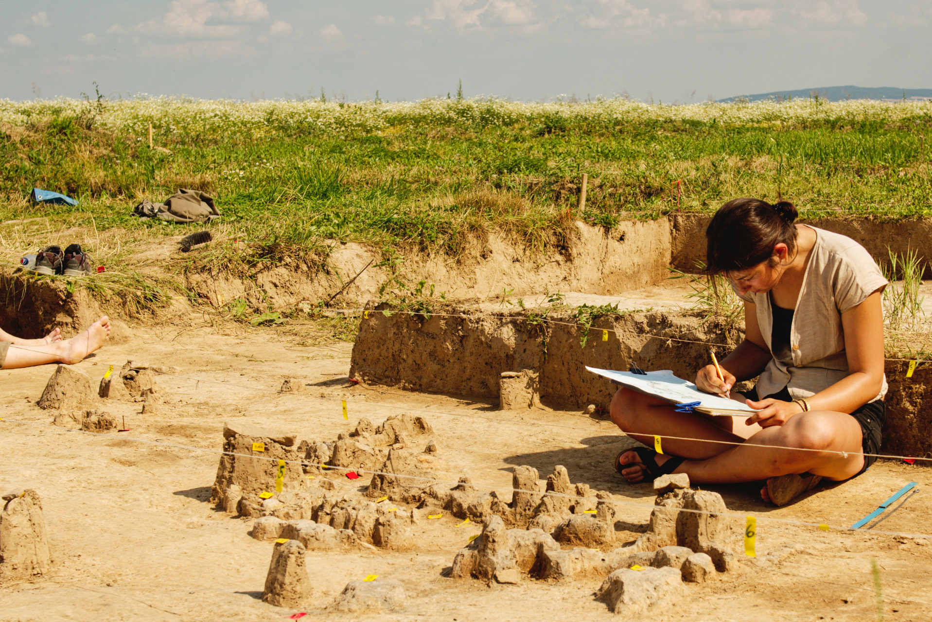 An archaeologist sitting on the ground, with a calm expression and a natural environment around her.