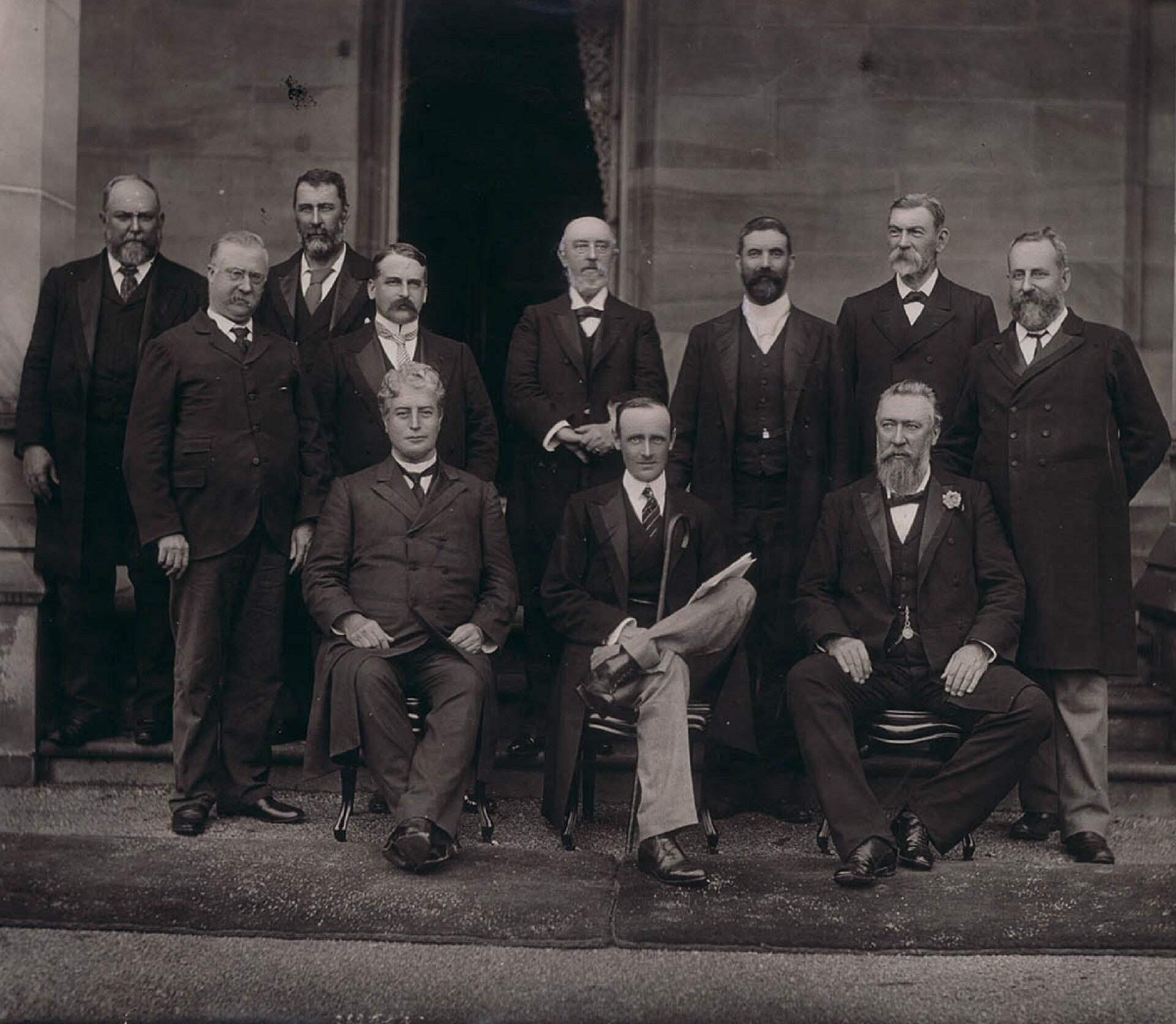 Men in suits, three of them seated, posing for a portrait.