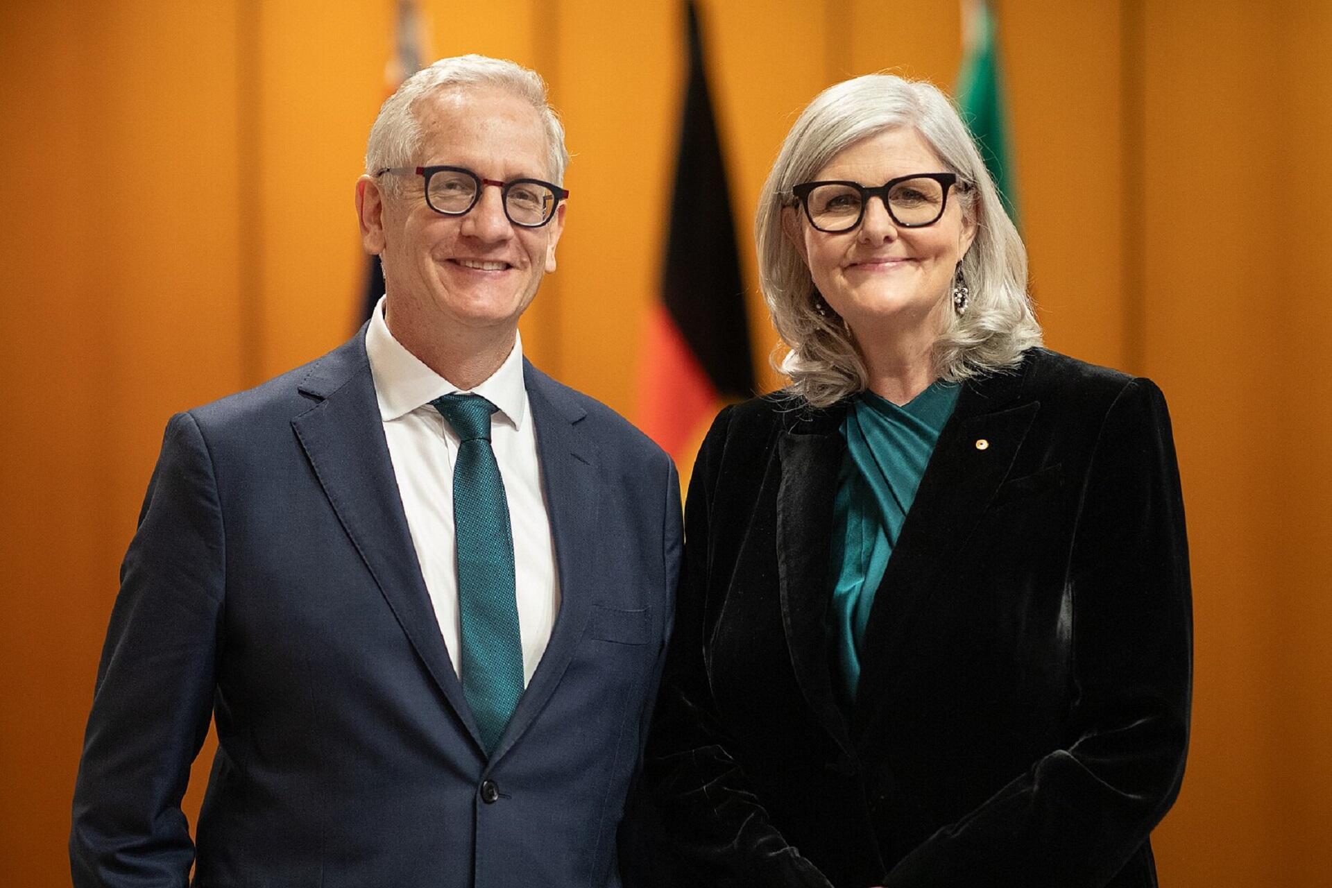 A man and woman posed before an orange background.