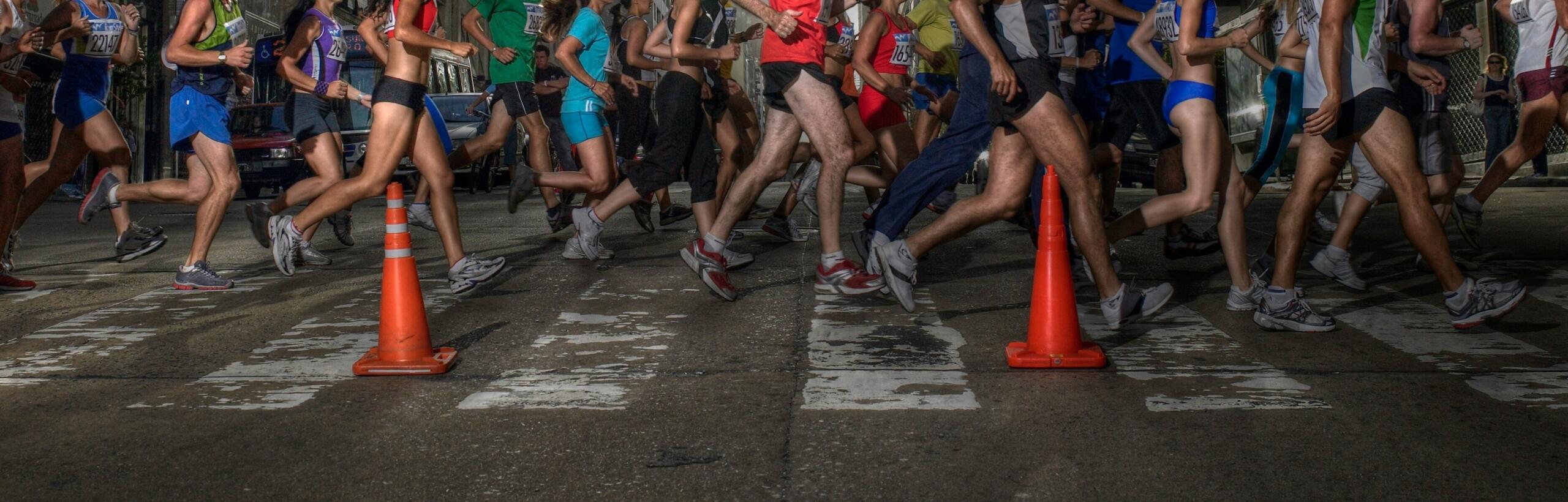 A dynamic scene of multiple runners in motion, crossing a street with orange traffic cones and a vivid urban backdrop.