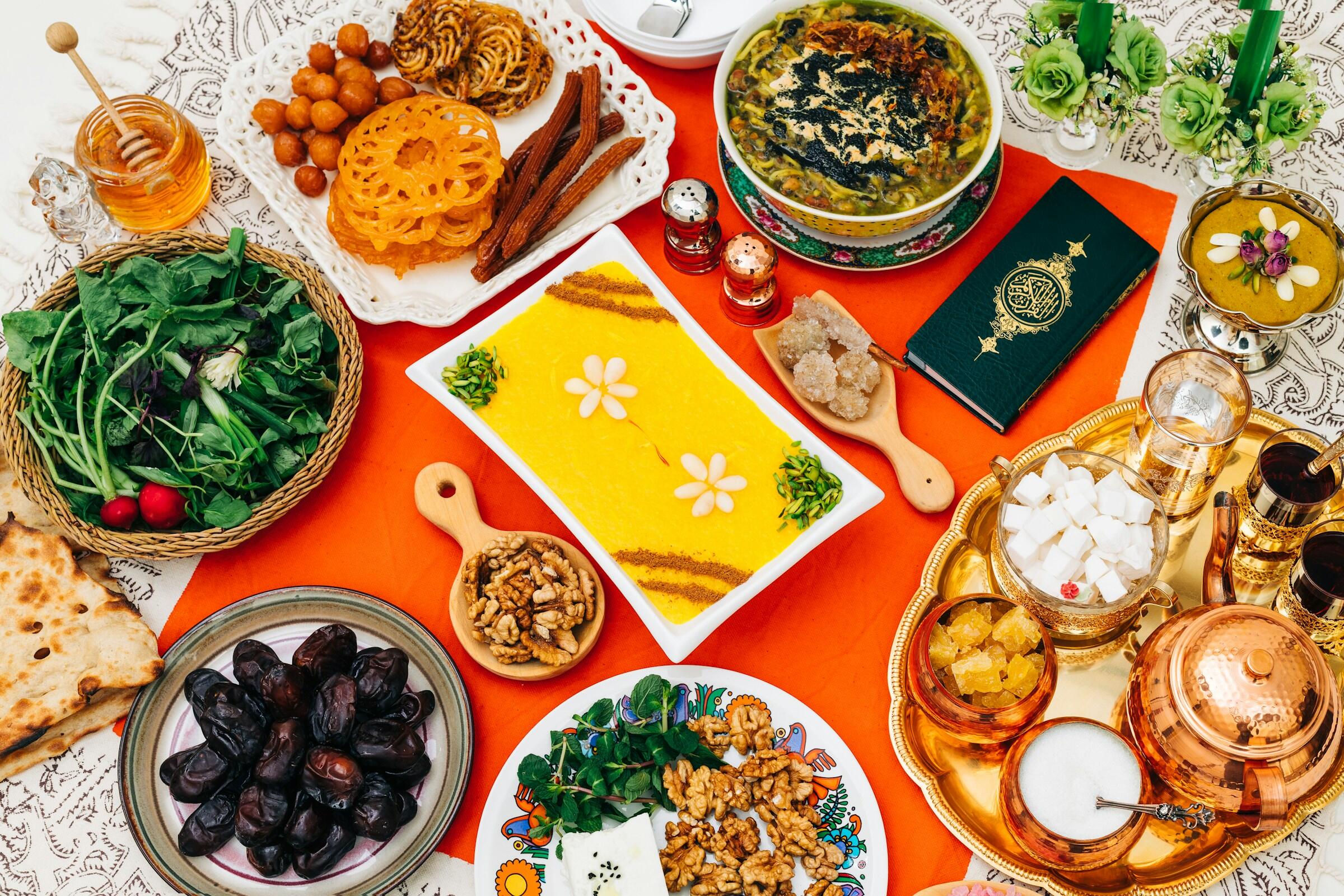 A spread of Middle Eastern dishes including sweets, salads, and traditional tea served on a tablecloth.