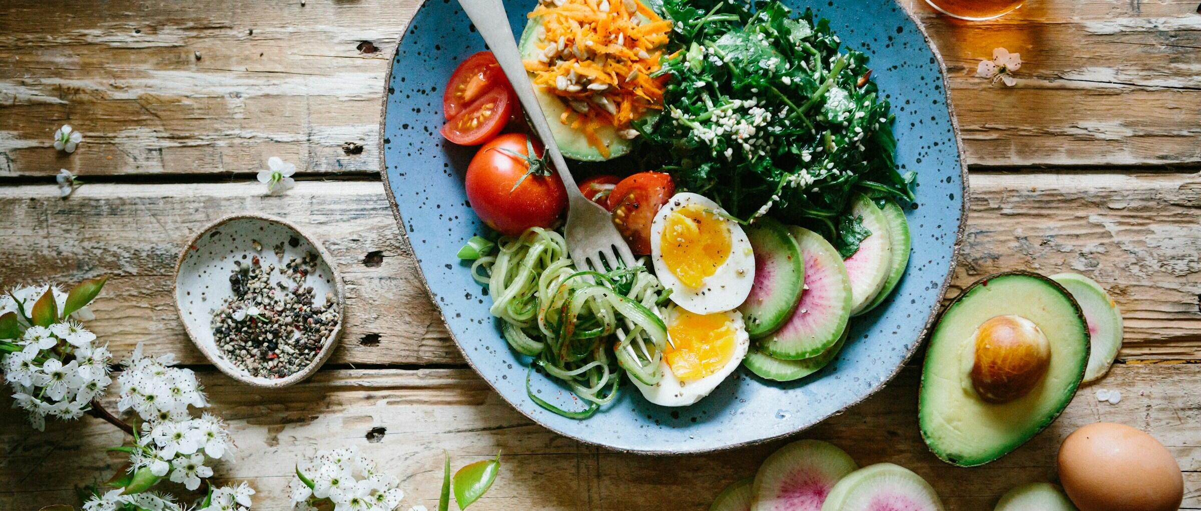 A colourful bowl of fresh vegetables, avocado, boiled eggs, and cherry tomatoes.