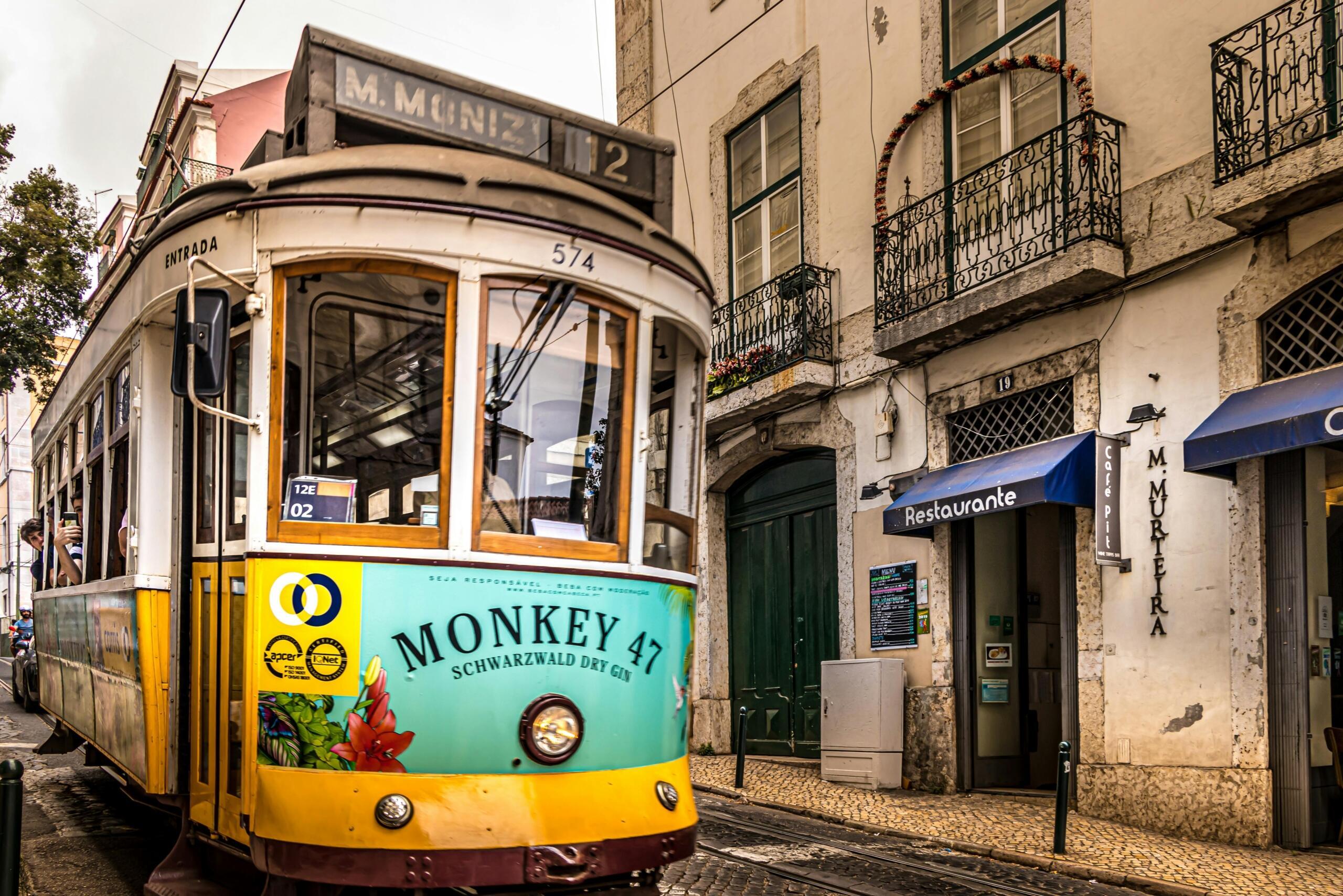 An antique yellow street car stands in front of an old building. A blue awning on the building says "restaurante".