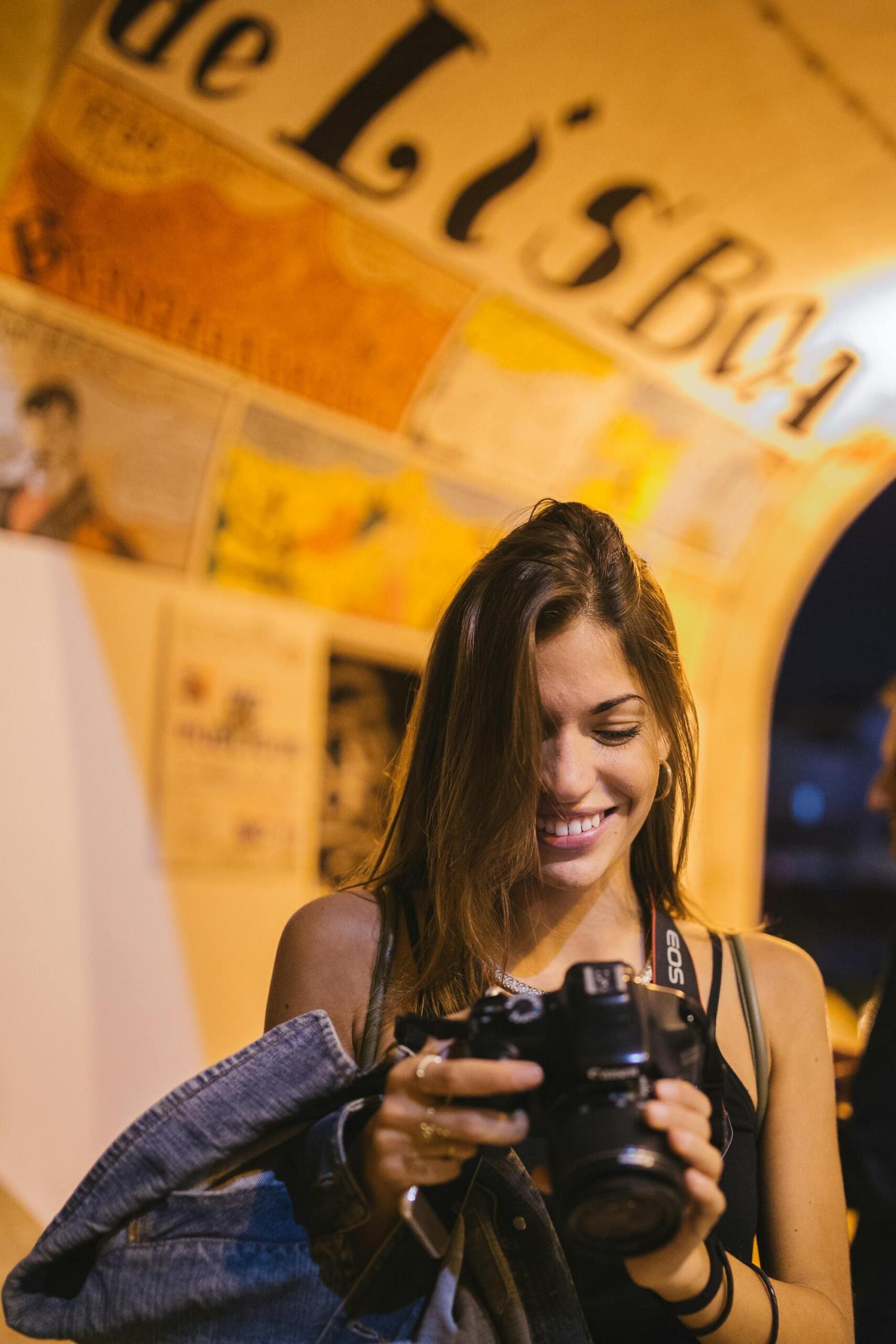 A woman looks into a large camera. On the ceiling, the text "Lisboa" can be seen. Source: Hillary Fox.