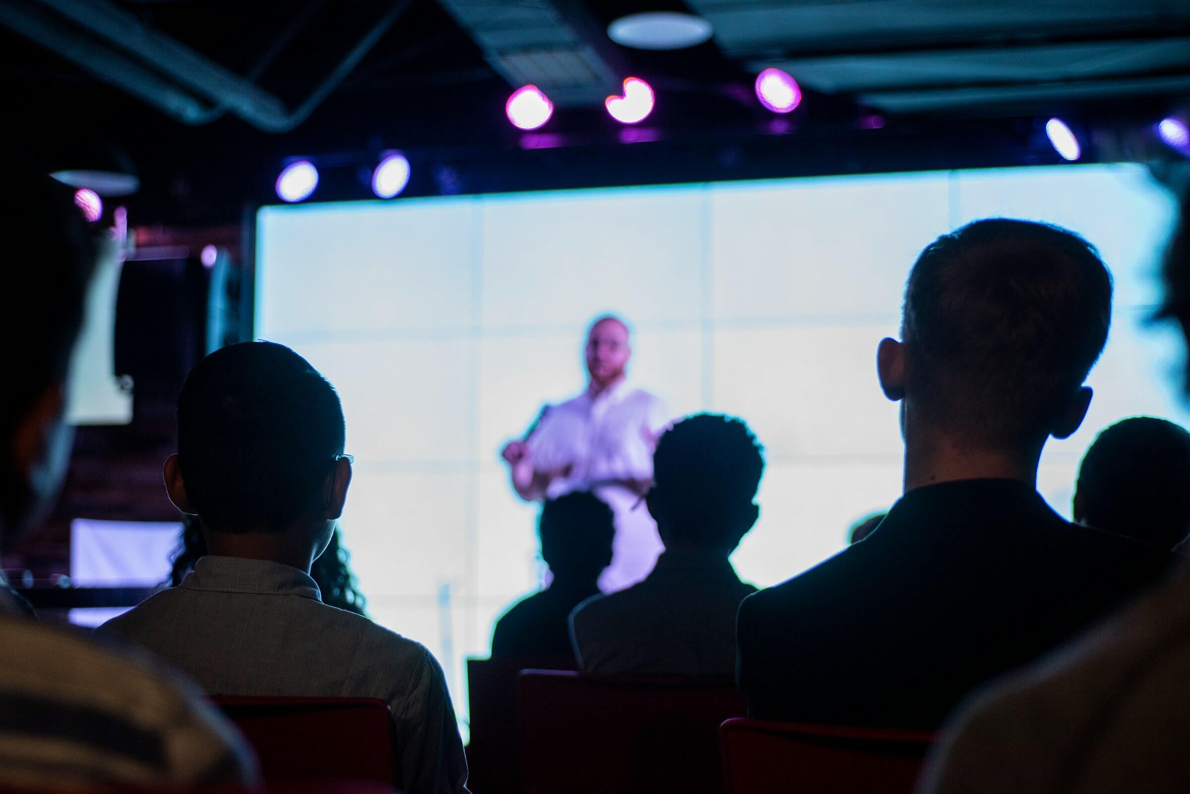 Audience members listening to a speaker on stage.