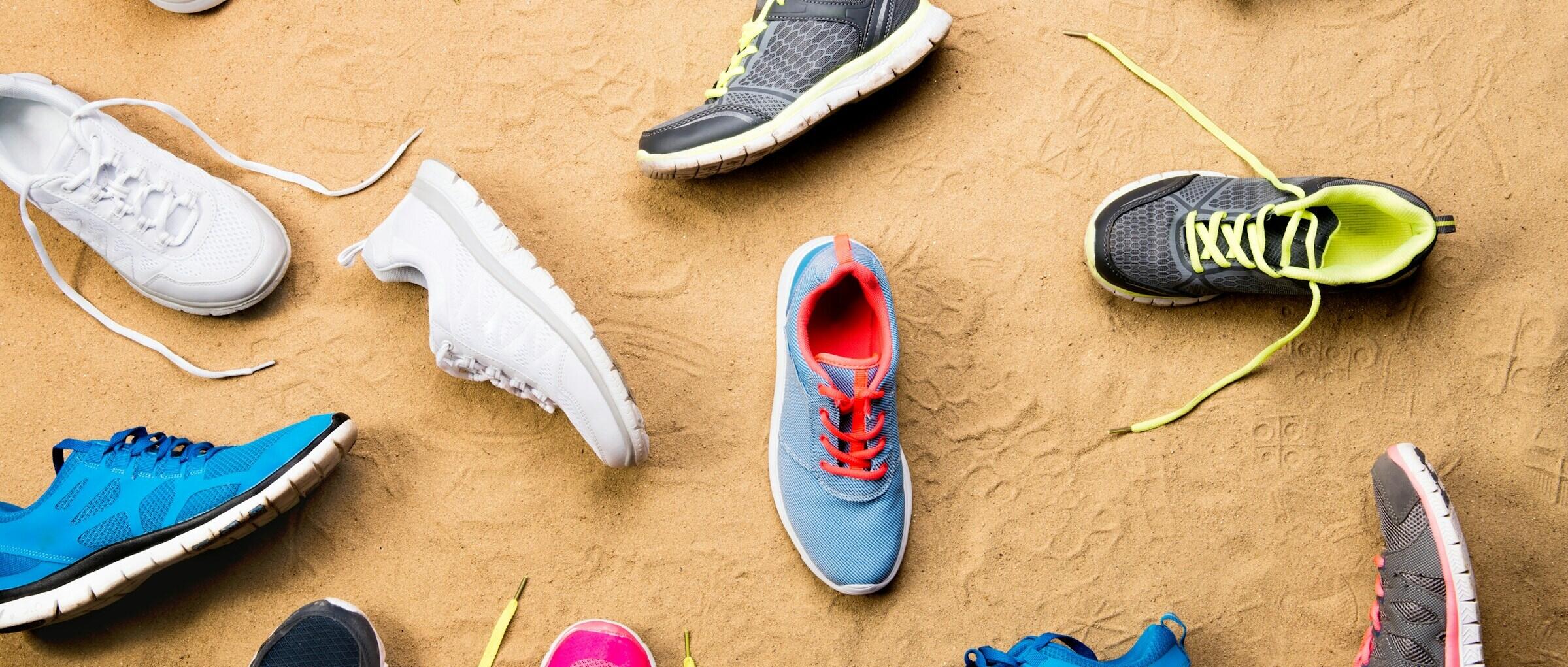 A cluster of colourful running shoes arranged on sandy ground.