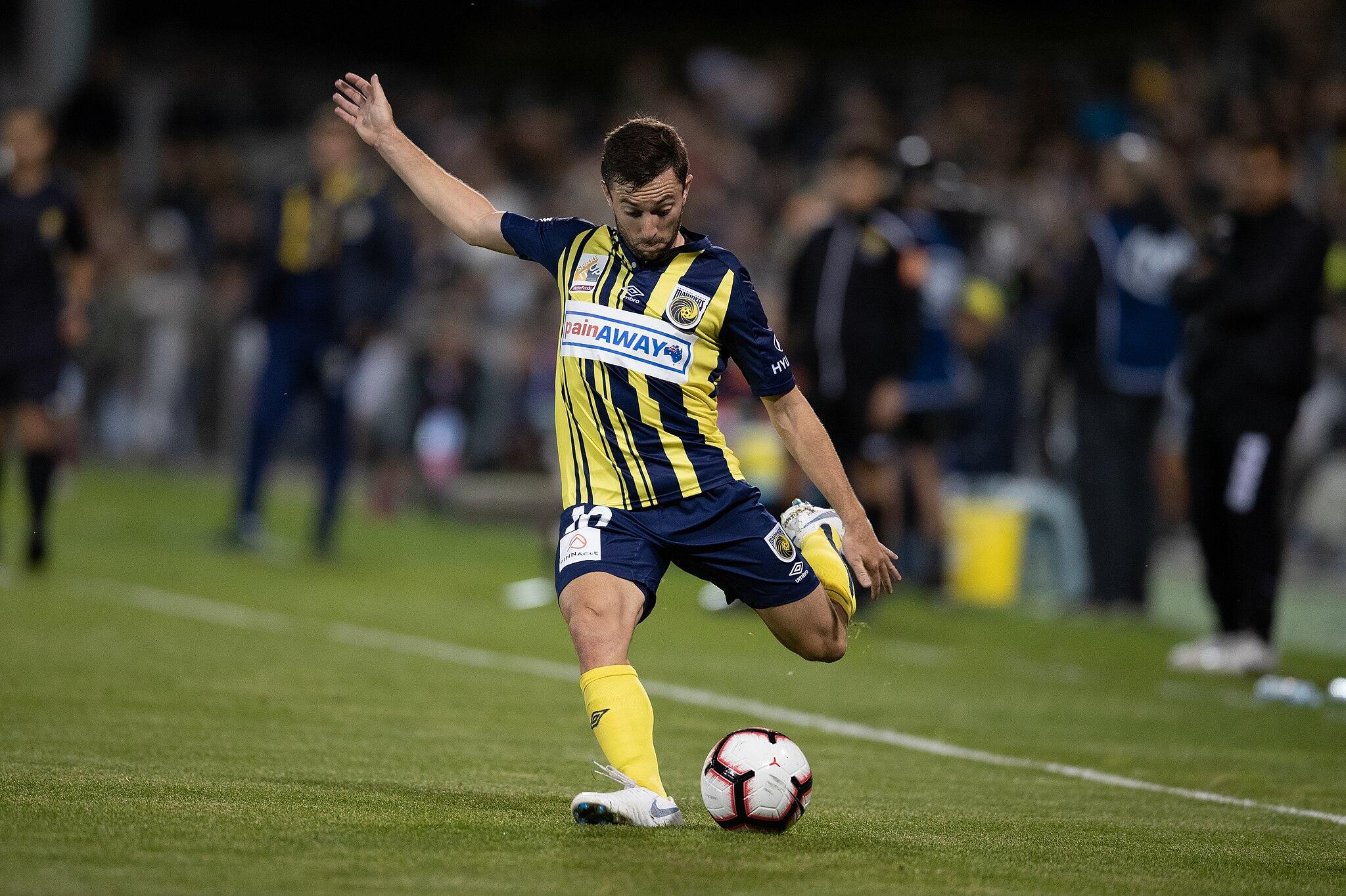 An Australian A League soccer player in a yellow and blue uniform prepares to kick the ball match.