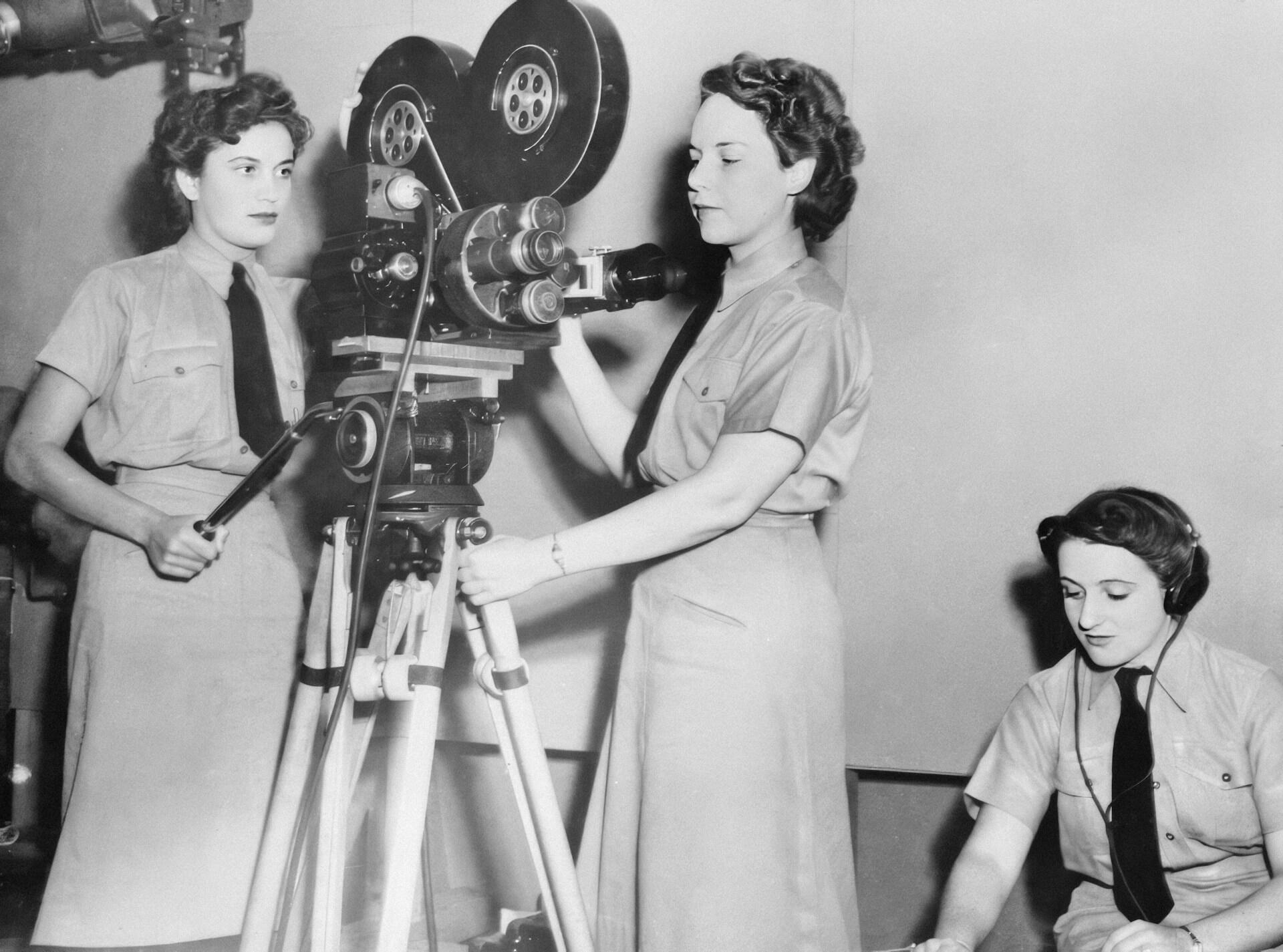 Two women set up a movie camera while another sits nearby.