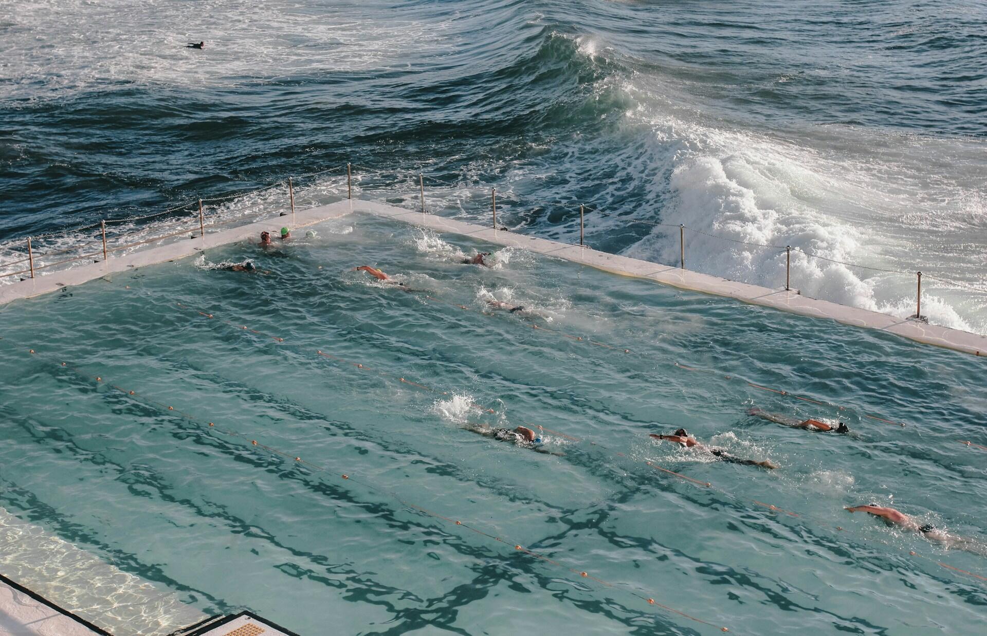 People swimming in a large ocean pool, surrounded by rolling waves.