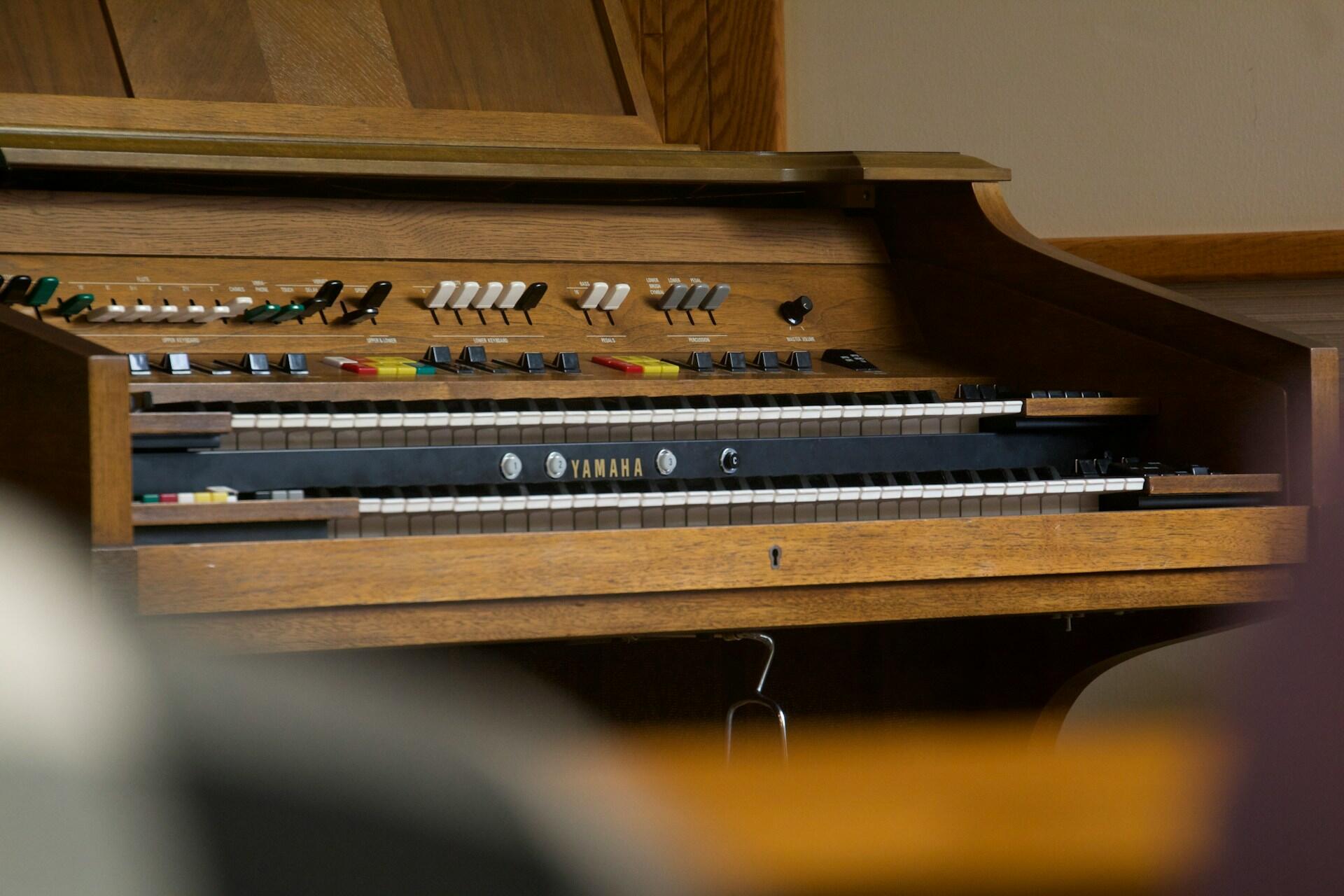 Close-up of a vintage Yamaha piano, showcasing its wooden design and various keys and buttons, in a warm-toned interior setting.