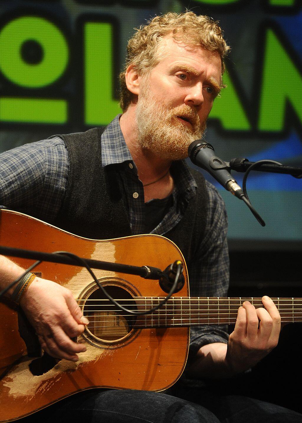 Irish singer Glen Hansard singing and playing the guitar on stage.