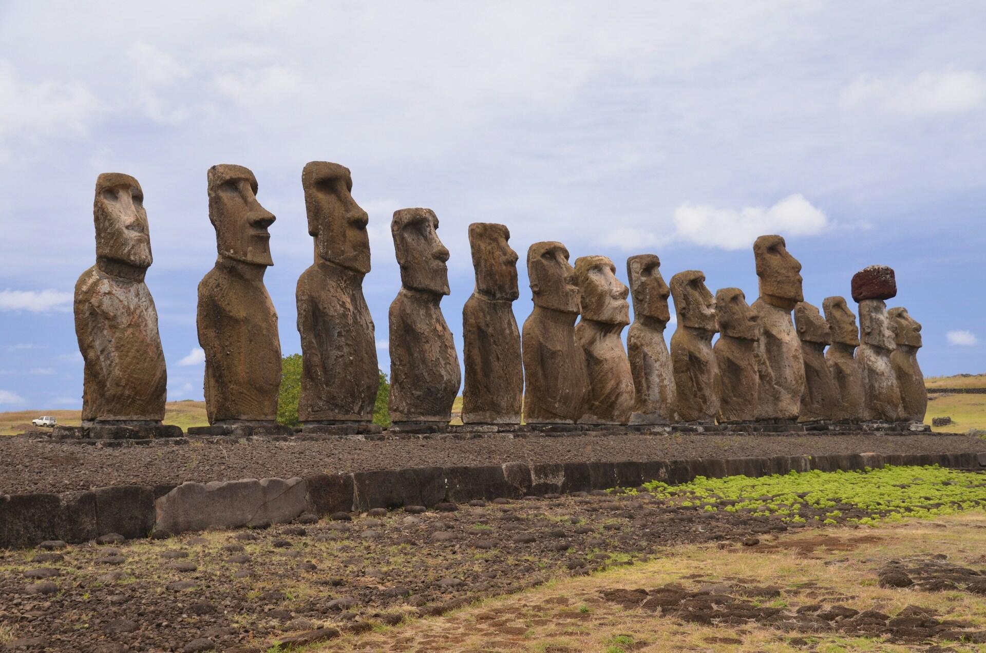 A row of Moai statues stands on Easter Island, framed by a cloudy sky and grassy earth.