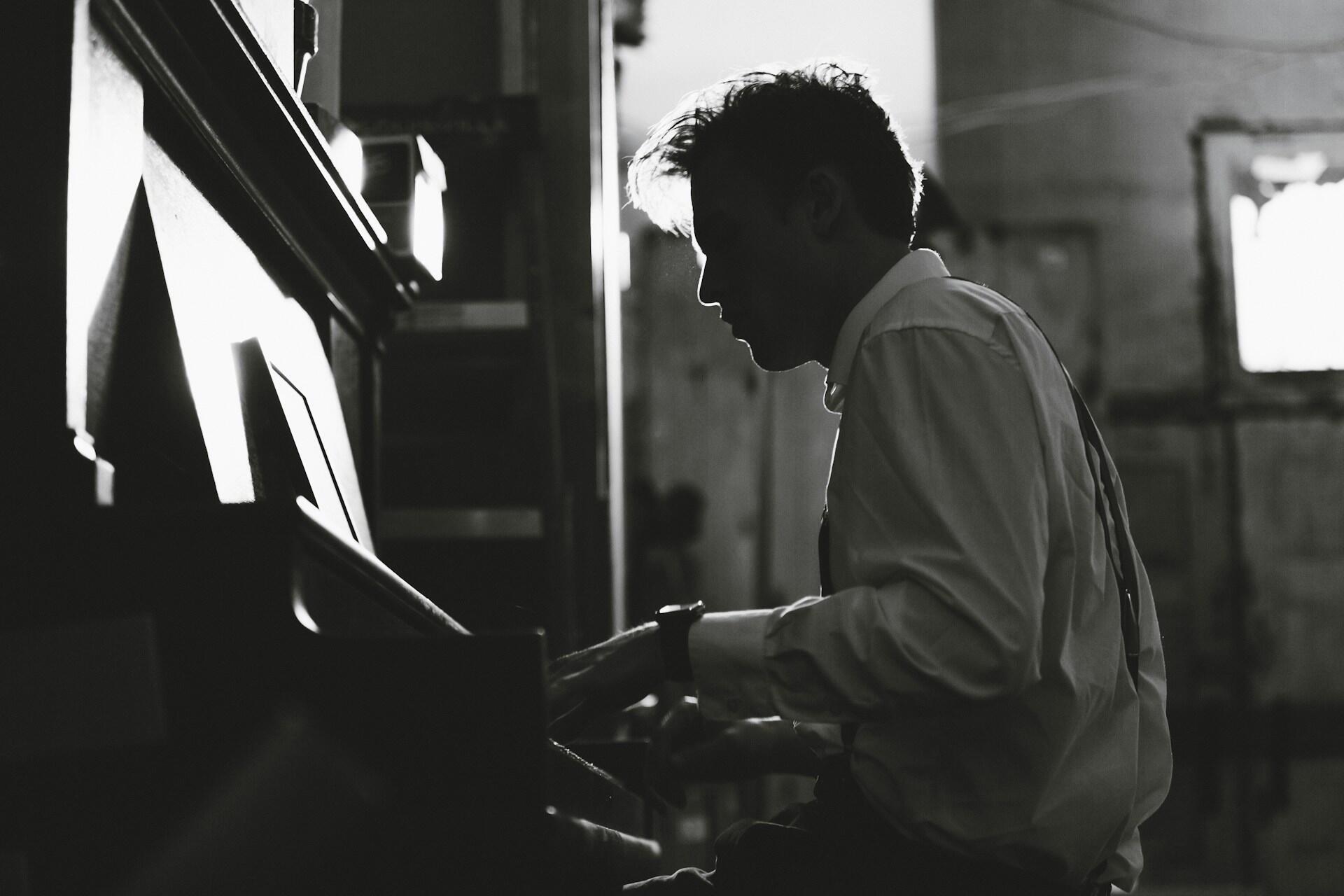 A person in a white shirt and suspenders plays a piano.
