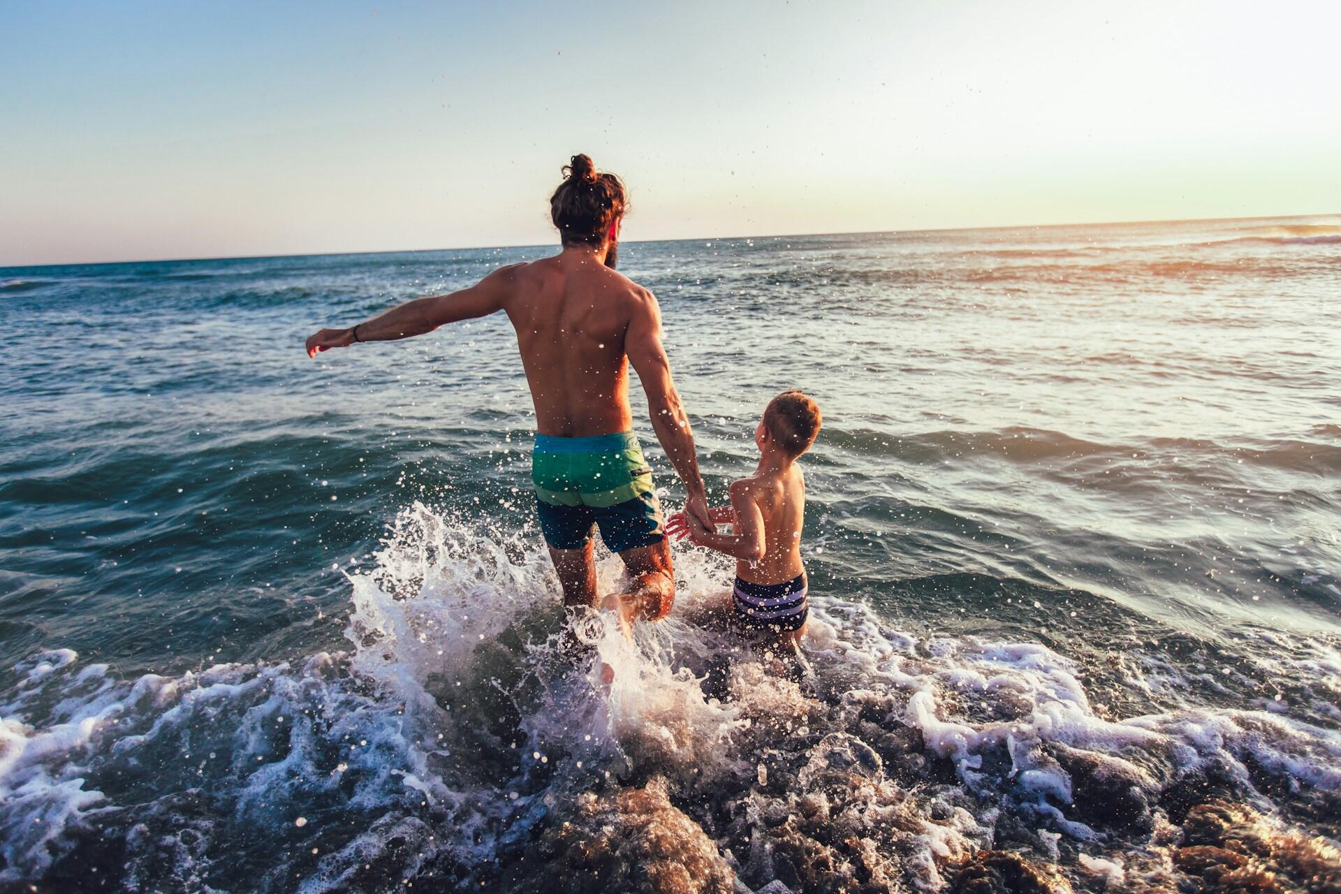 A man and a child joyfully splash through the waves at sunset.
