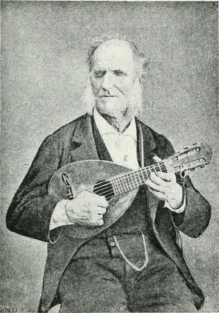 An old photo of a man playing an early guitar