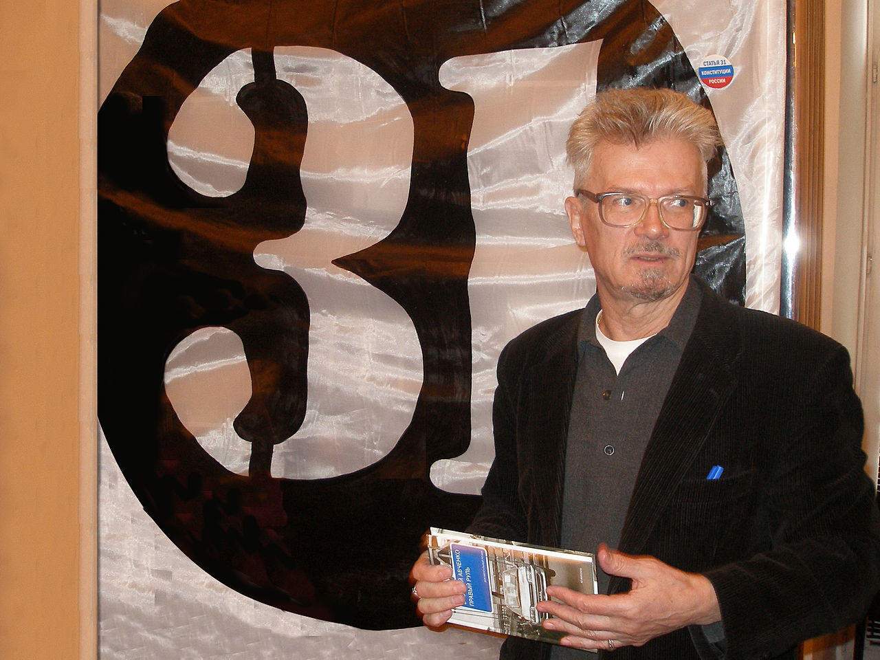 A person stands holding a book in front of a large banner.