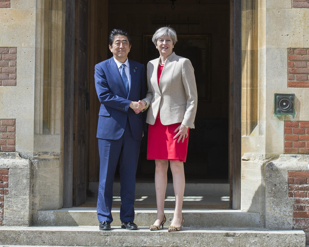 A man in a blue suit and a woman in a red dress shake hands on the steps of a historic brick building.