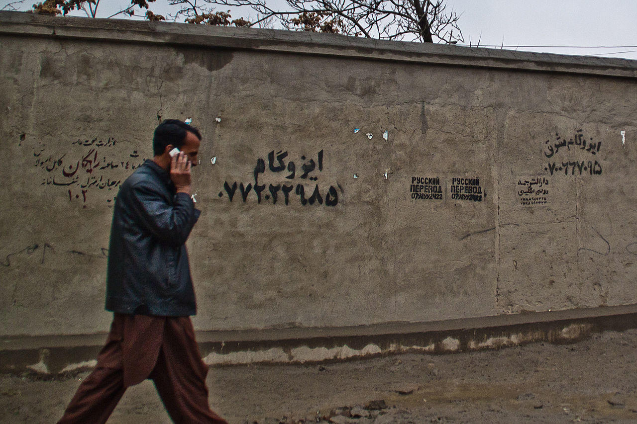 A person walks past a gray wall covered in handwritten and printed advertisements.