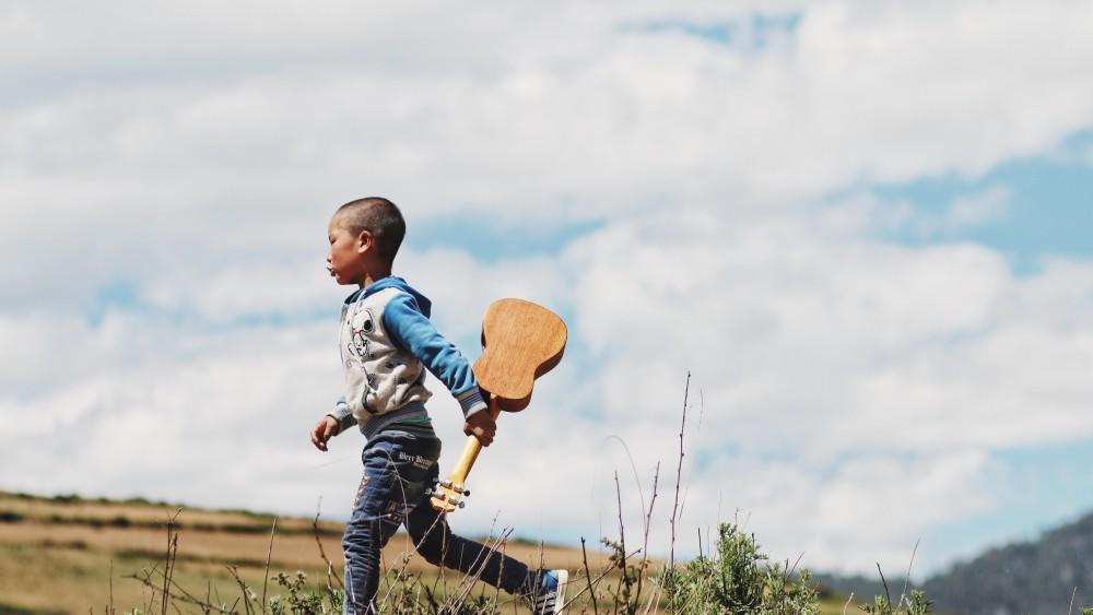 A child runs in a field with a guitar