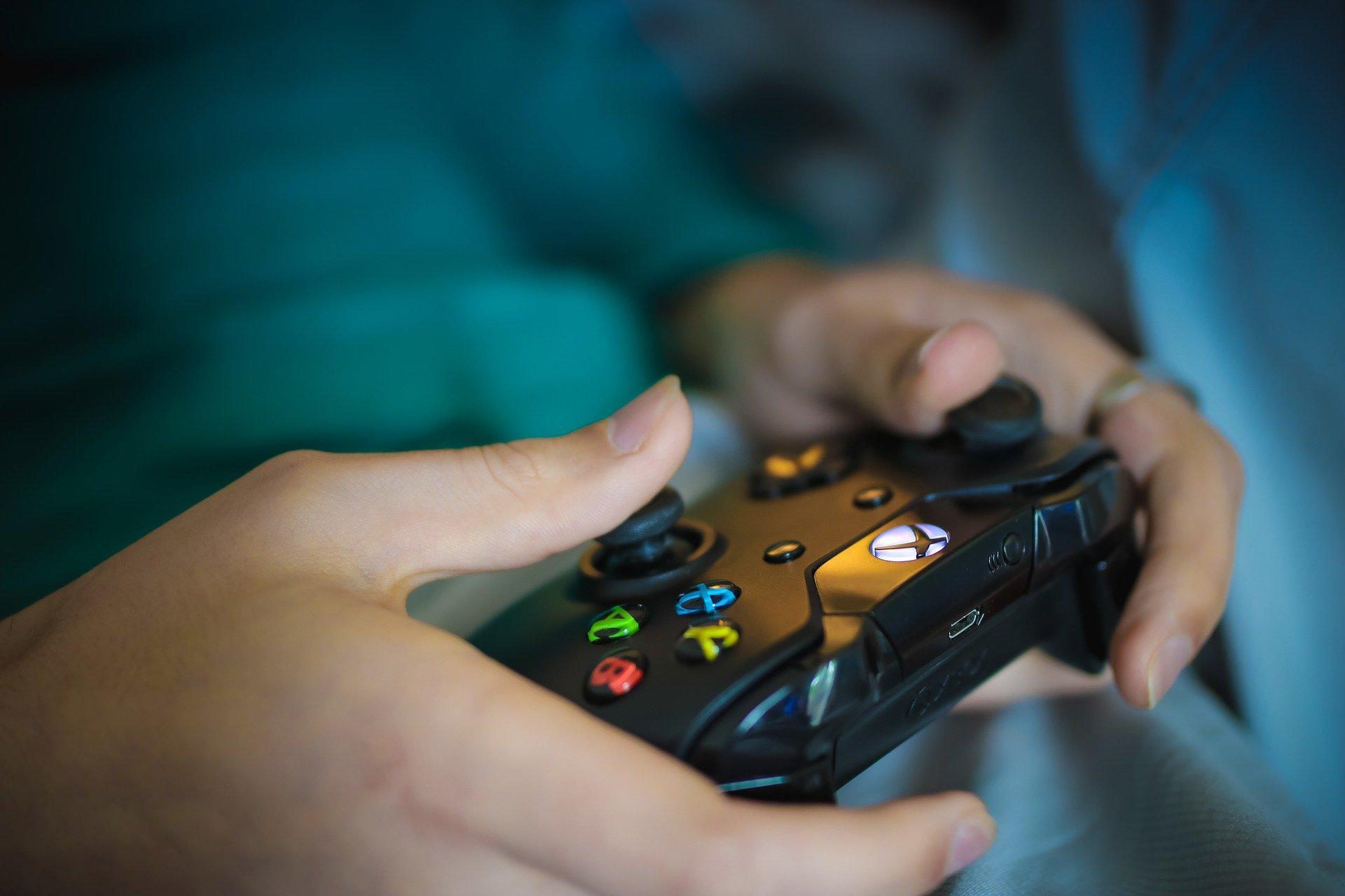 A person wearing a teal shirt holding a black XBox controller with their thumbs on the joysticks, activating the left-side one.