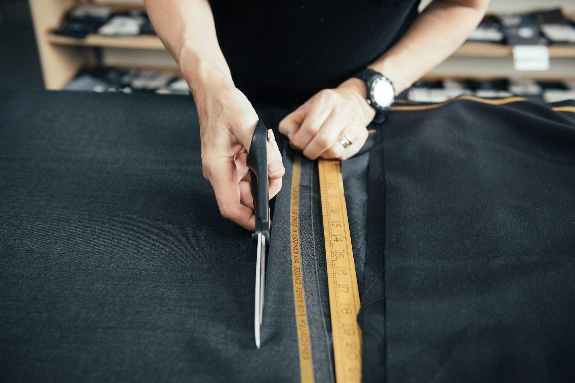 Person cutting fabric with scissors beside a measuring ruler on dark textile material