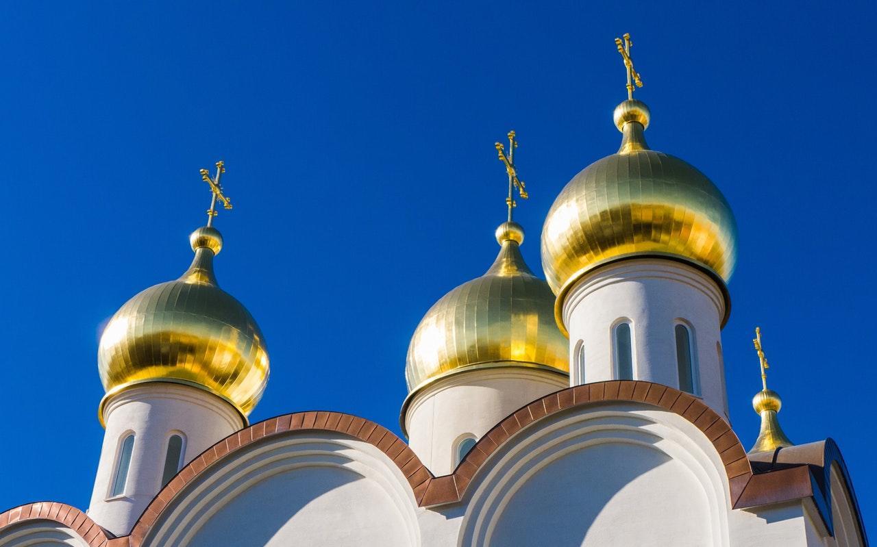 Three golden onion domes topped with crosses against a bright blue sky.