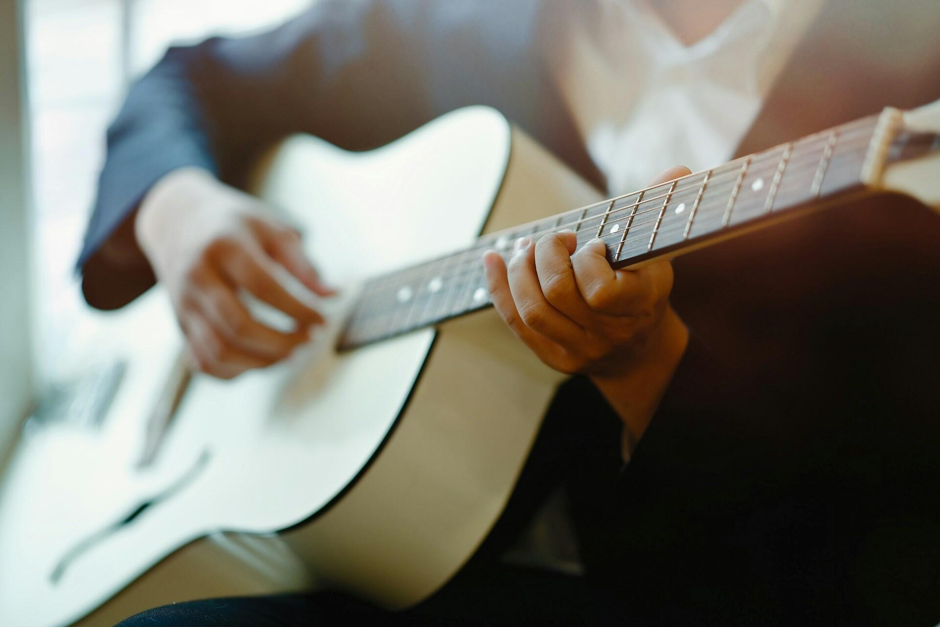 A close-up of a person’s hands playing a white acoustic guitar.