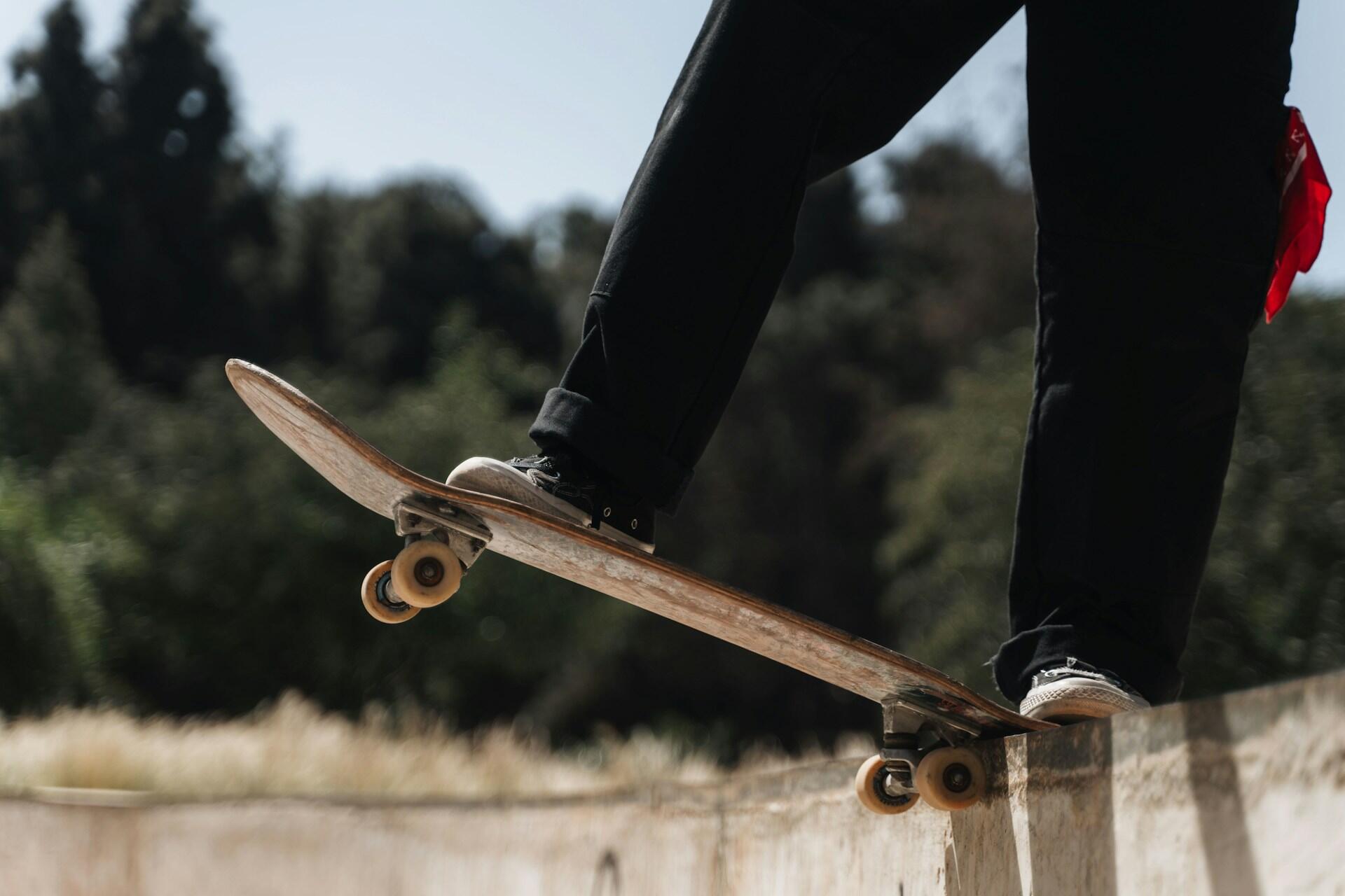 A skateboarder balances on the edge of a ledge, wearing black pants and sneakers, with a blurred green background behind them.