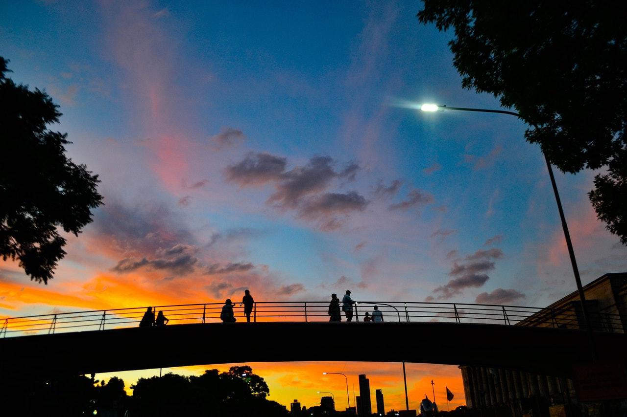 Silhouettes of people on a bridge against a vibrant sunset with colourful clouds.