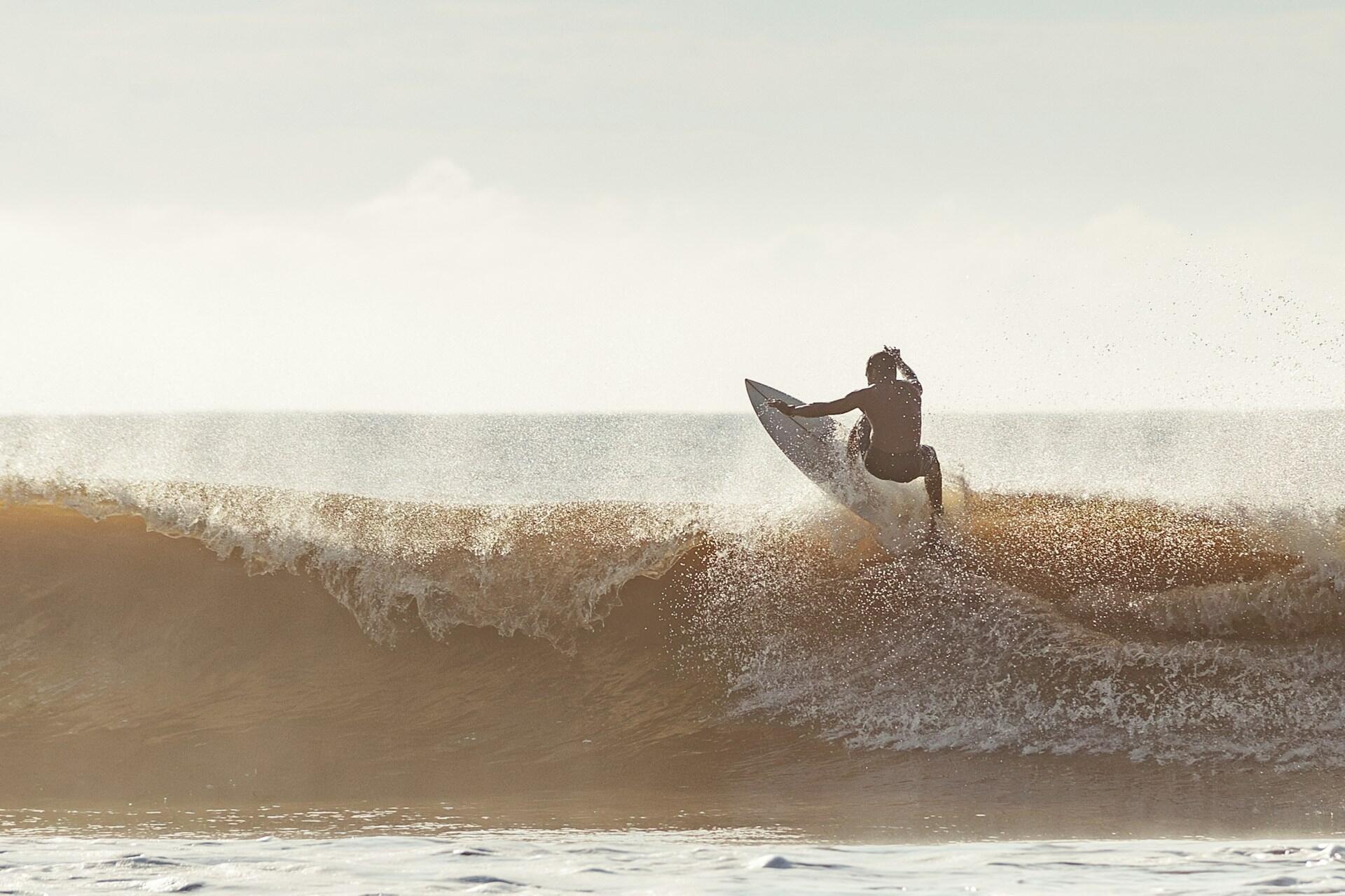 A surfer surfing on a wave under a bright sky.